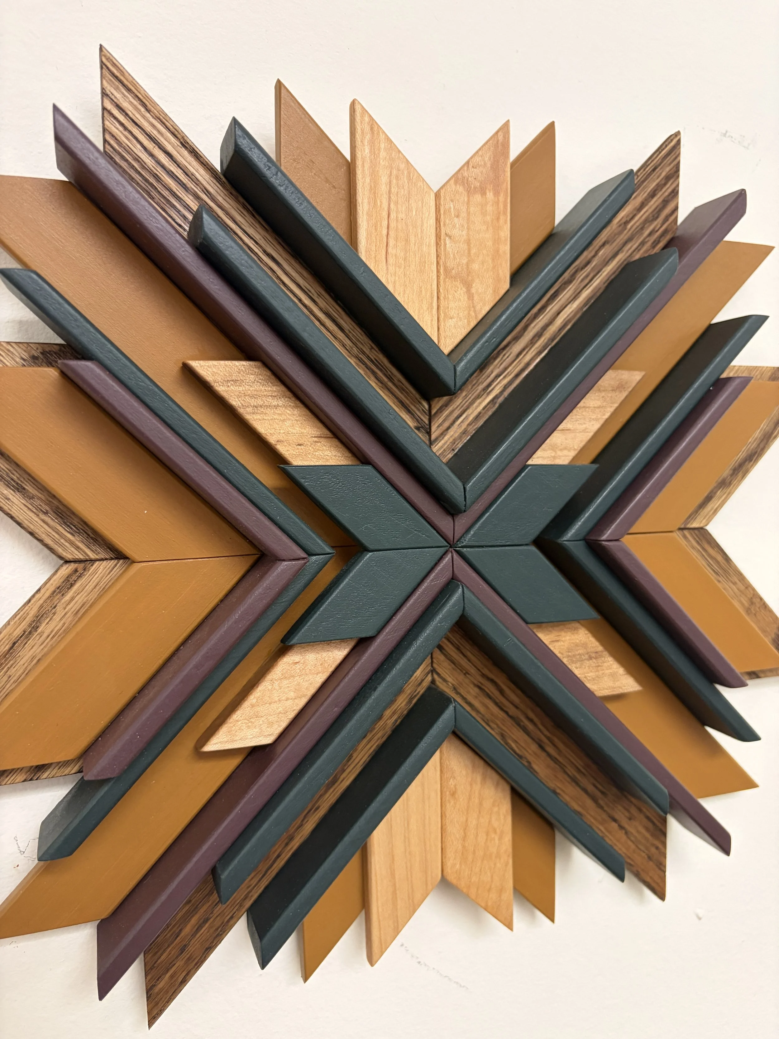 Close up view of a wooden sunburst style mosaic in purple, green, and yellow paint with natural and espresso stains.