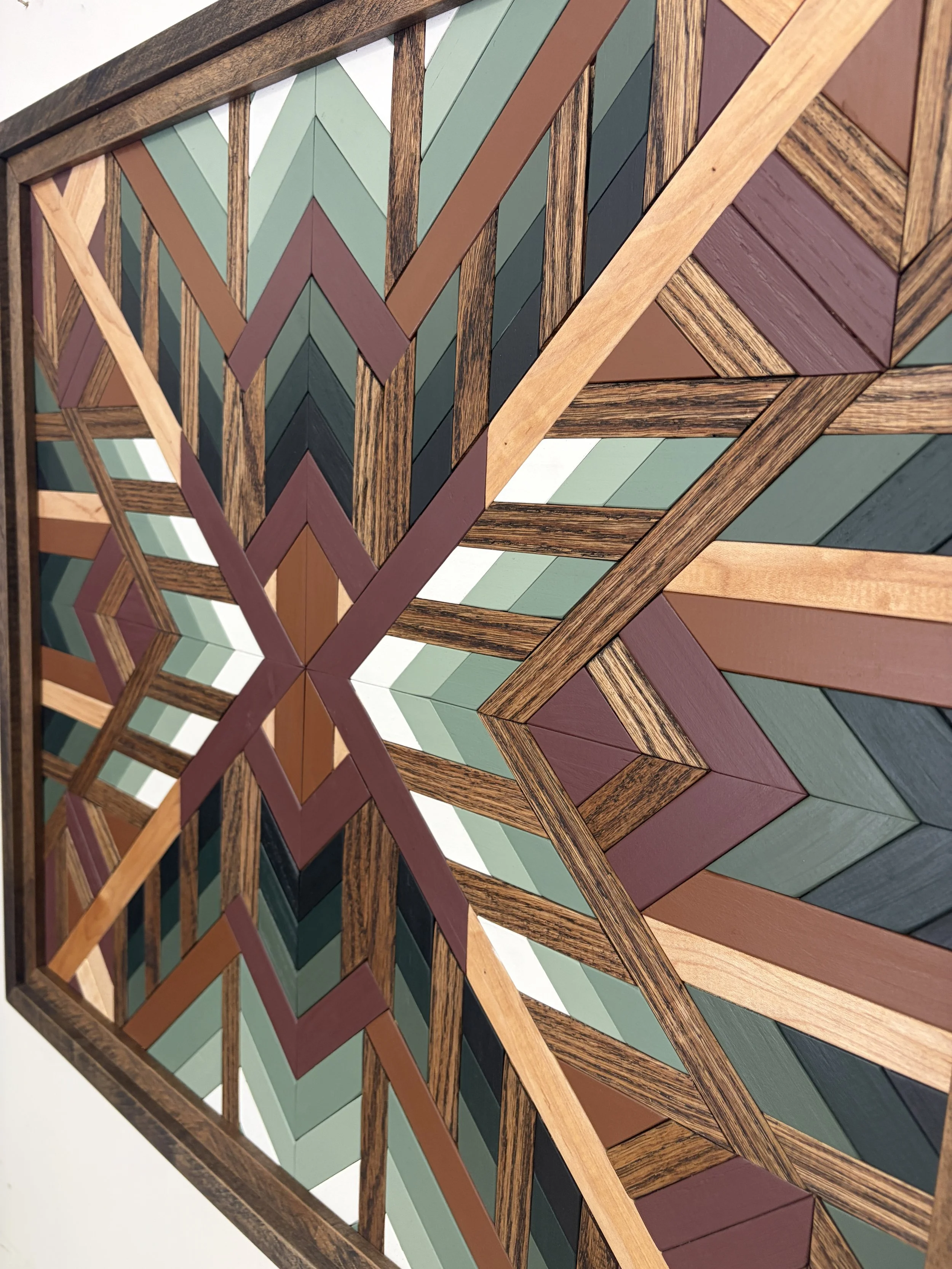 Close up side view of a handcrafted framed wooden mosaic in black, white, pink, orange, and various green paints with natural and espresso stains.