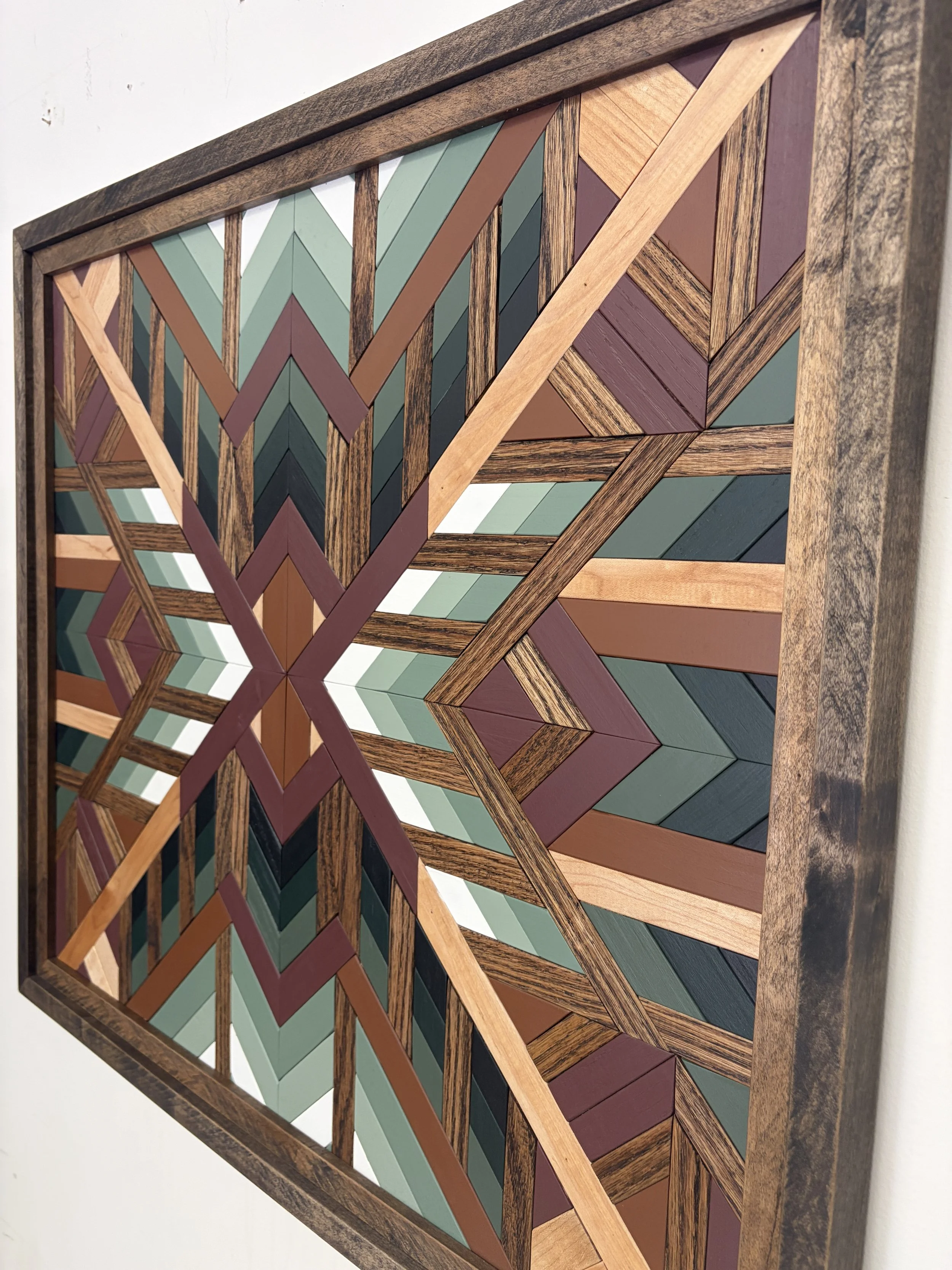 Side view of a handcrafted framed wooden mosaic in black, white, pink, orange, and various green paints with natural and espresso stains.