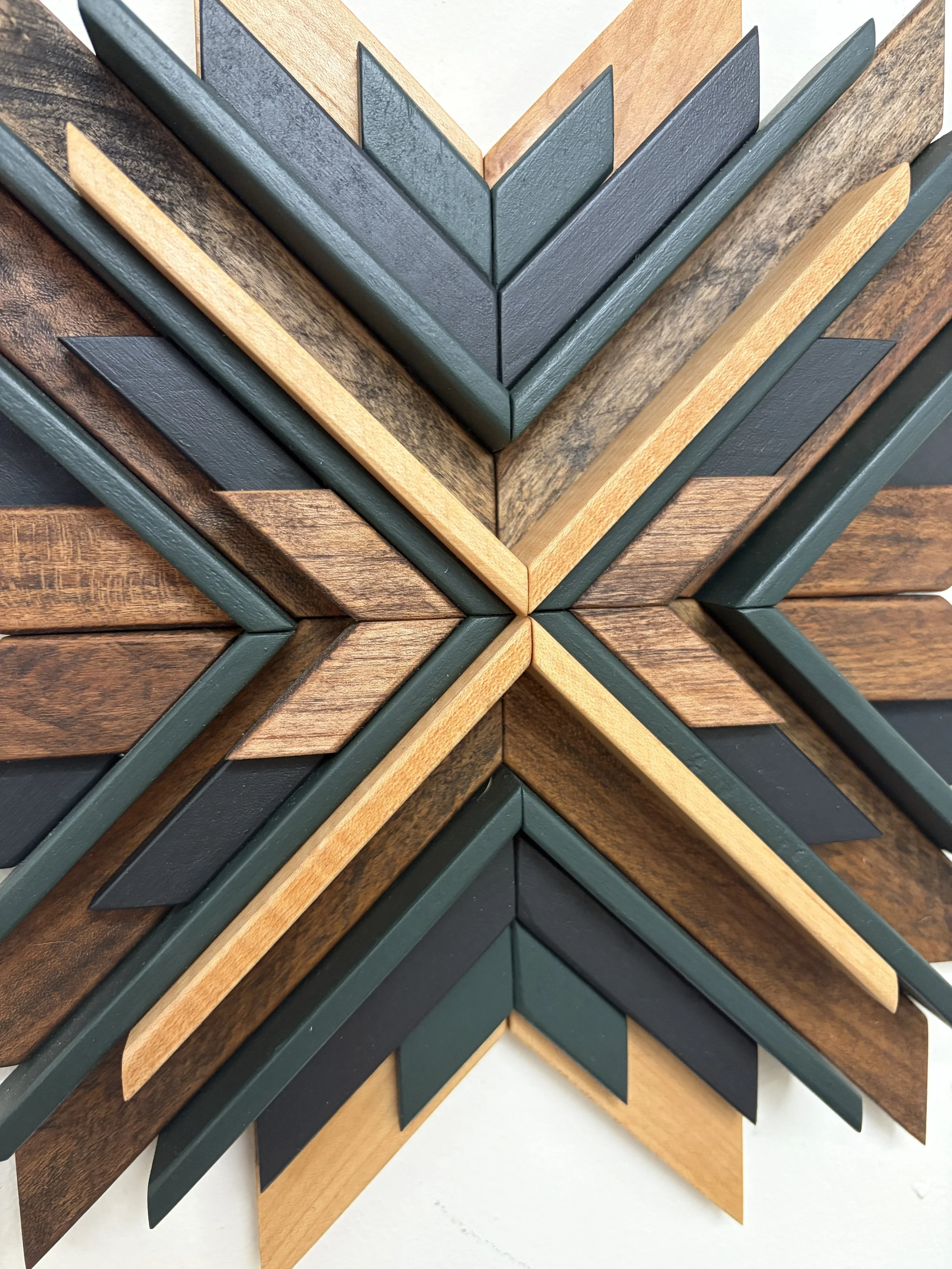 Close up view of a wooden sunburst style mosaic in black and green paint with natural and espresso stains.