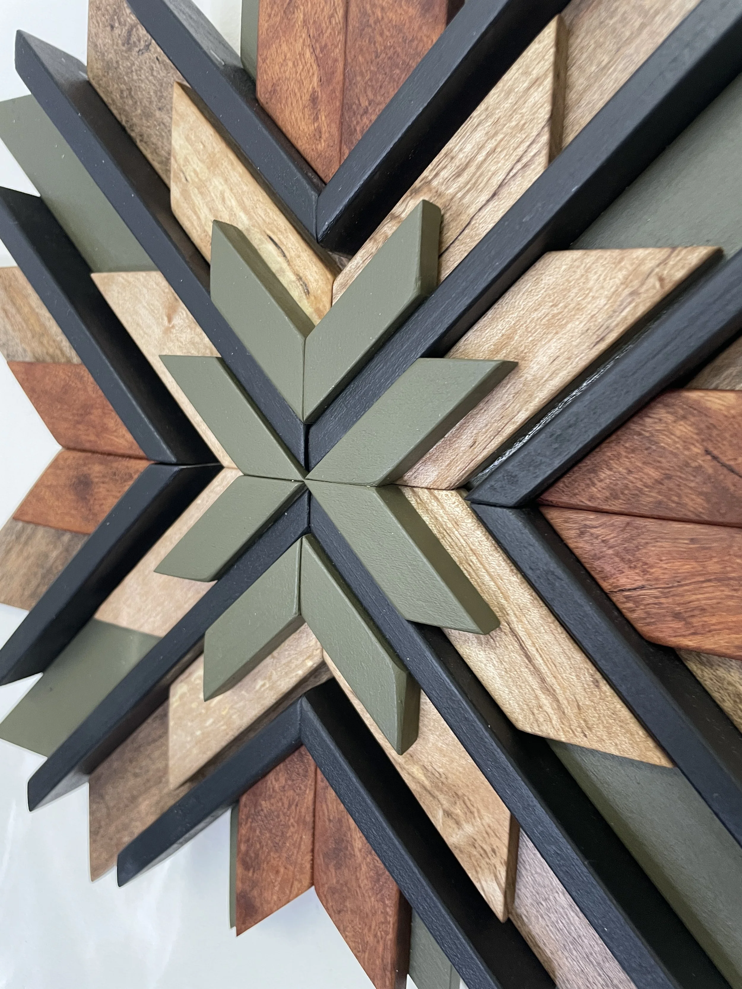 Close up view of a handcrafted sunburst style wooden mosaic in black and green paint with natural and dark wood stains.