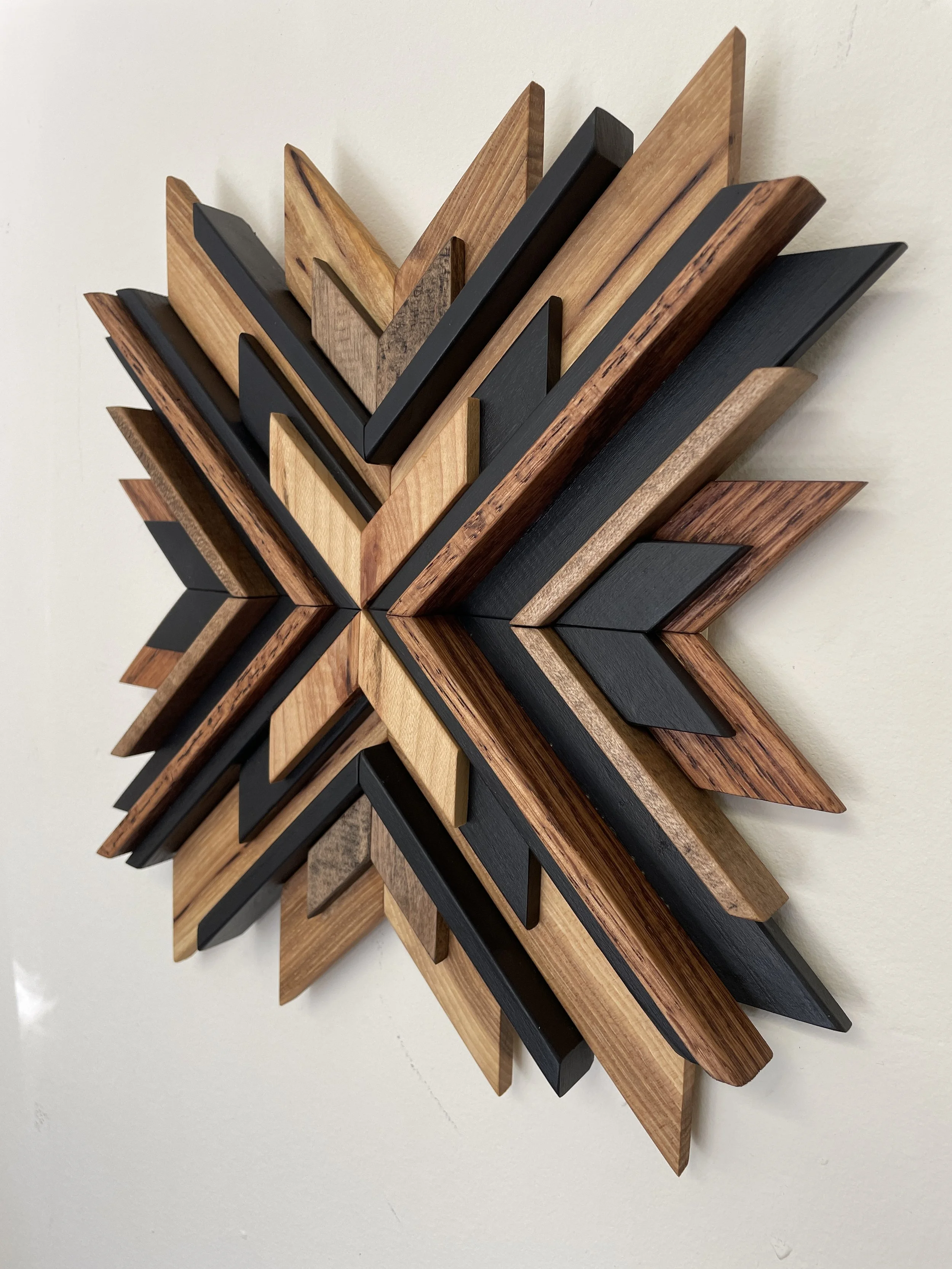 Angled view of a handcrafted sunburst style wooden mosaic in black paint with natural, espresso, and red mahogany stains.