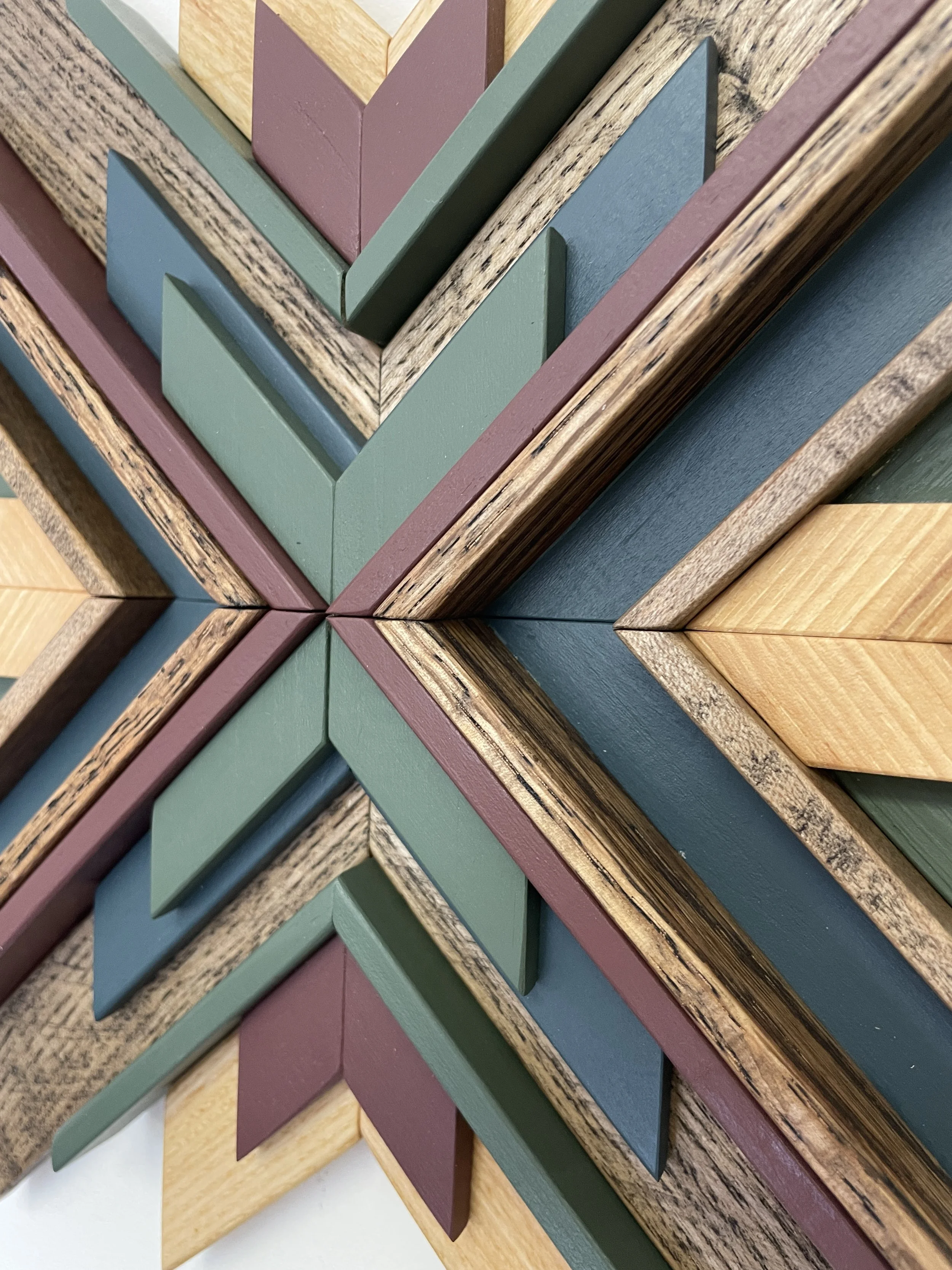 Close up view of a handcrafted sunburst style wooden mosaic in pink, green, and blue paints with natural and espresso stains.
