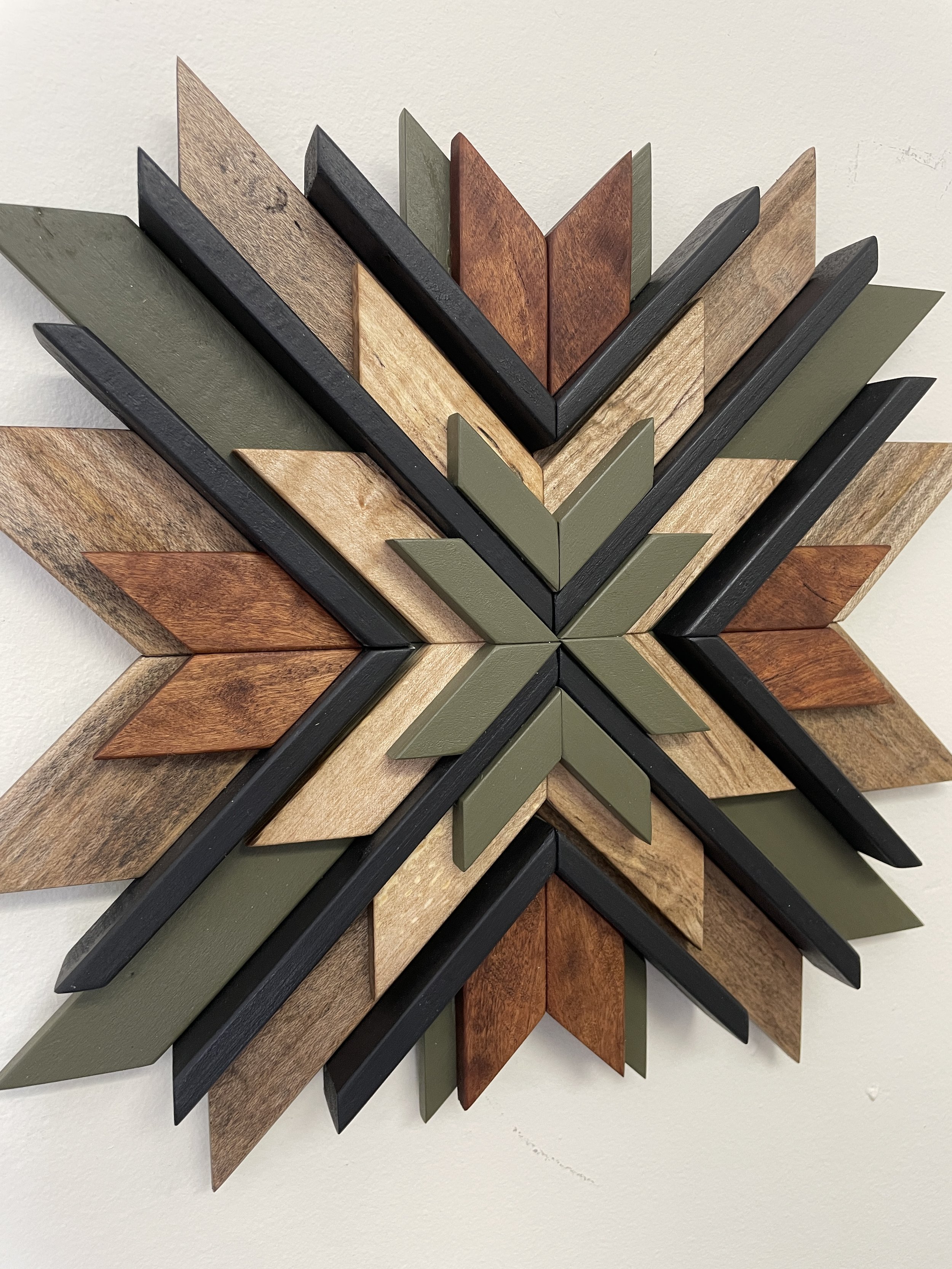 Angled view of a handcrafted wooden sunburst mosaic in black and green paints with natural and espresso stains.