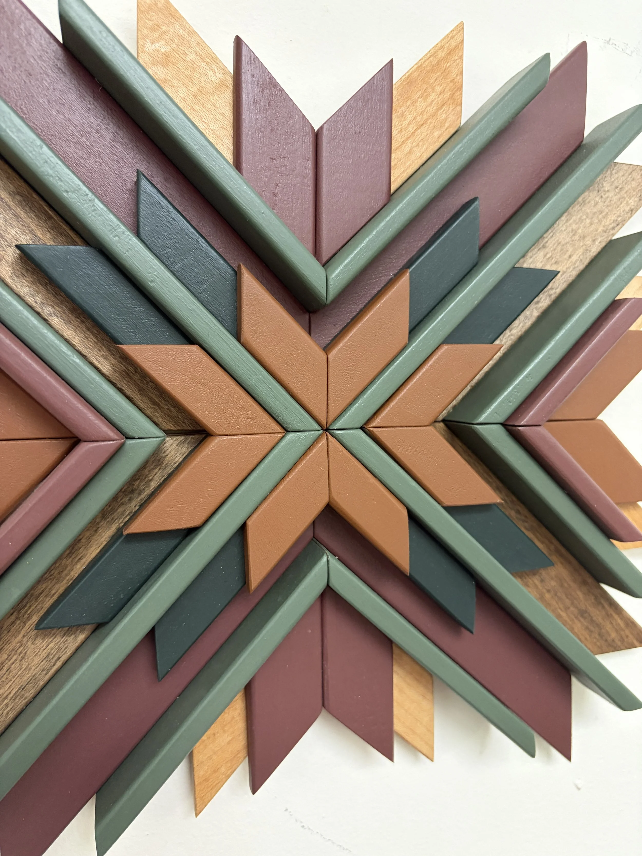 Close up view of a wooden sunburst style mosaic in pink, orange, and green paint with natural and espresso stains.