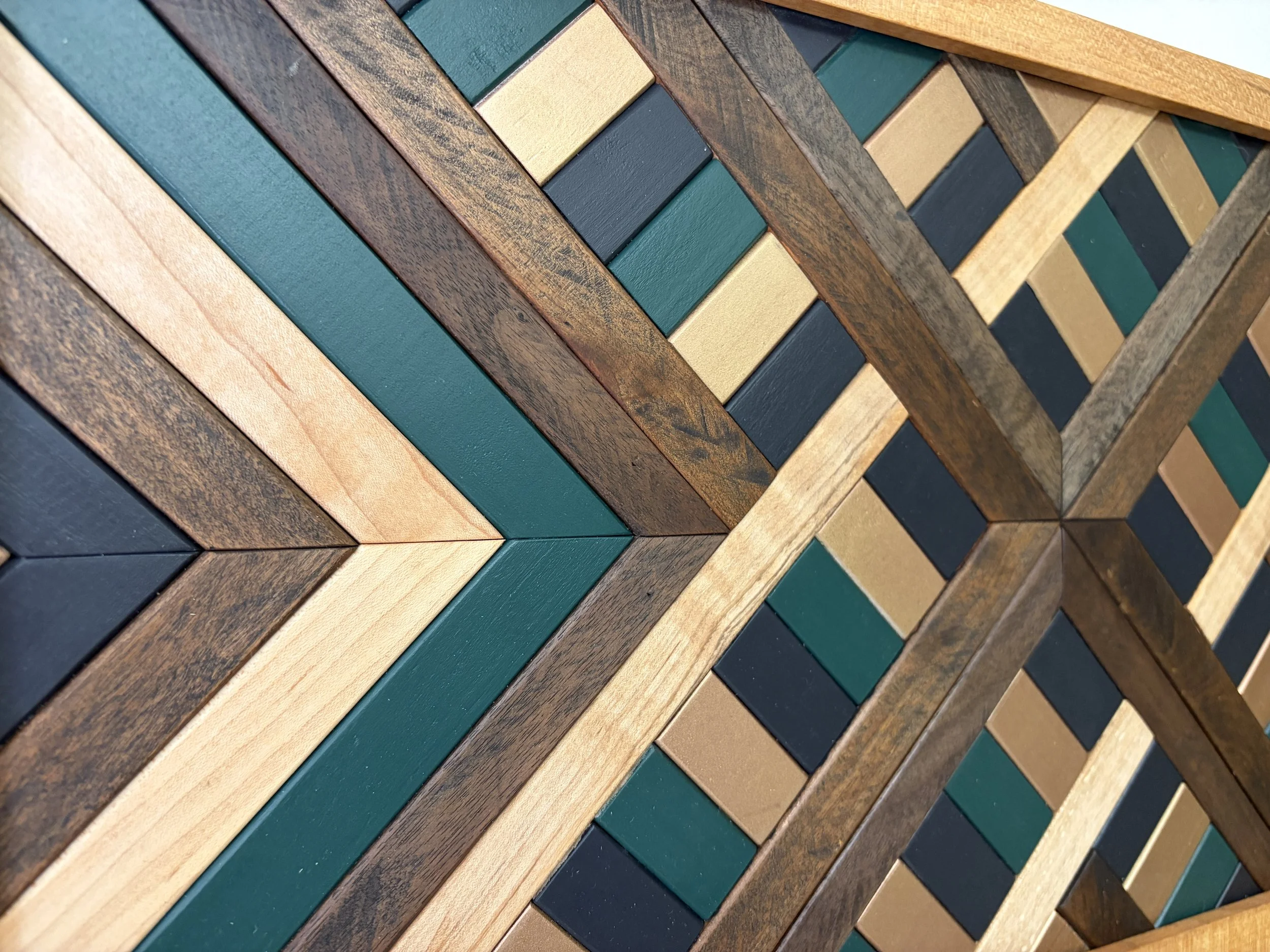 Close up view of a handcrafted framed wooden mosaic in black, green, and gold paint with natural and espresso stains.