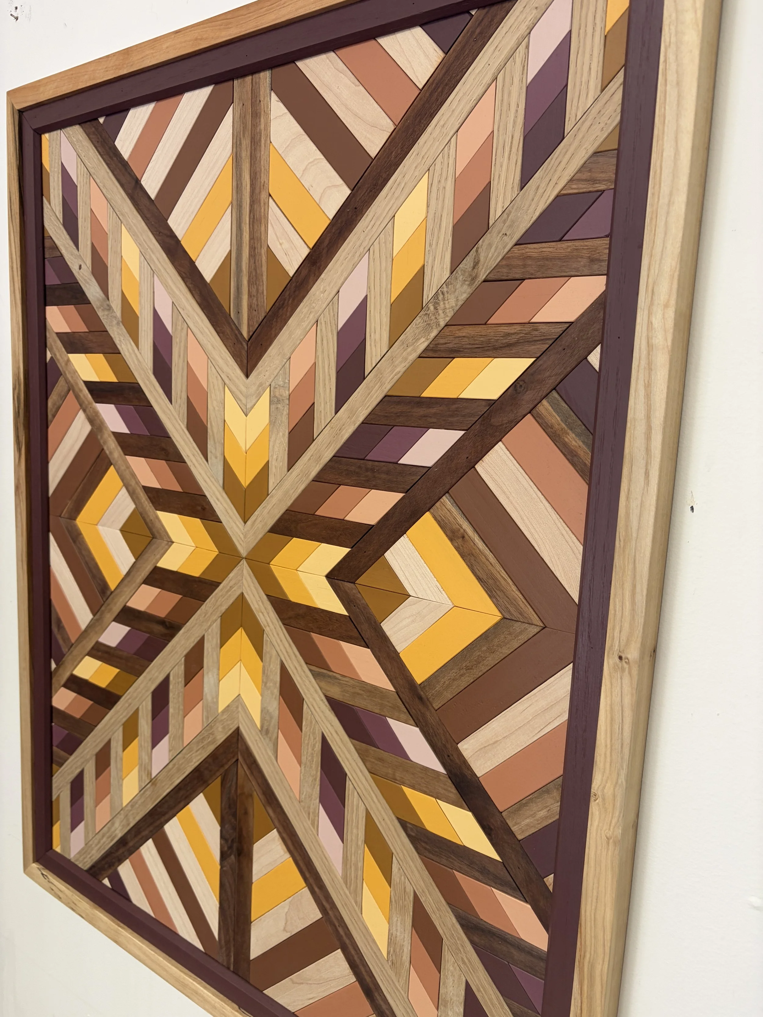 Angled view of a handcrafted framed wooden mosaic in several shades of pink, orange, and yellow paint with natural stains.