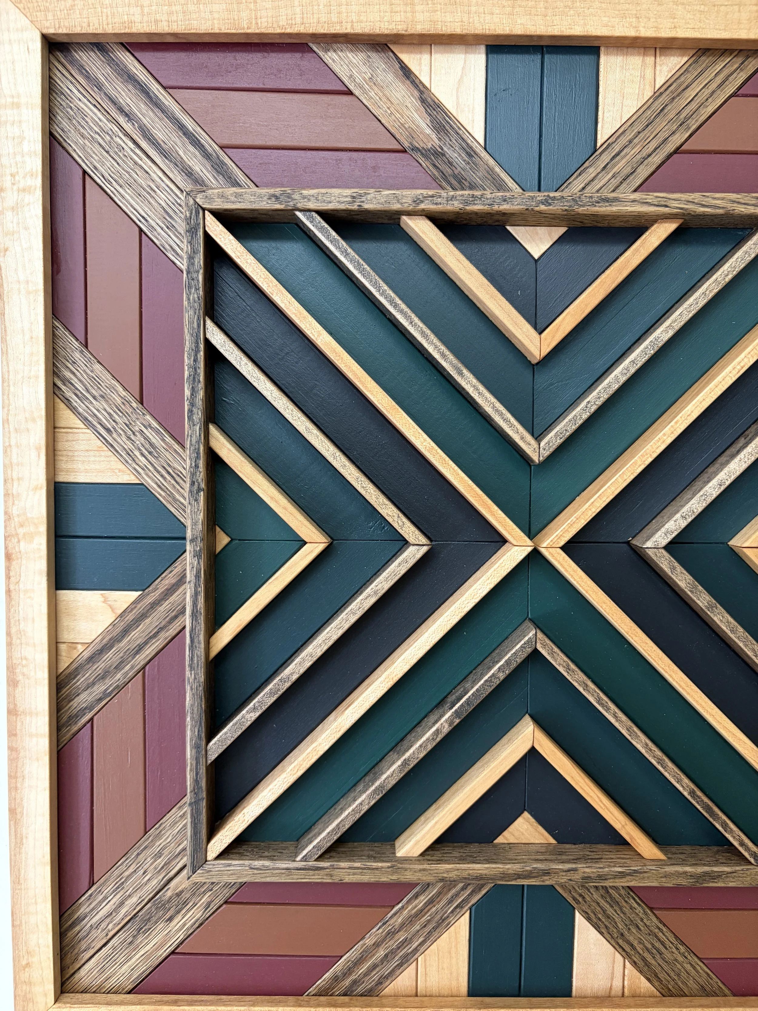 Close up view of a handcrafted framed wooden mosaic in black, green, teal, pink, and orange paint with natural and espresso stains.