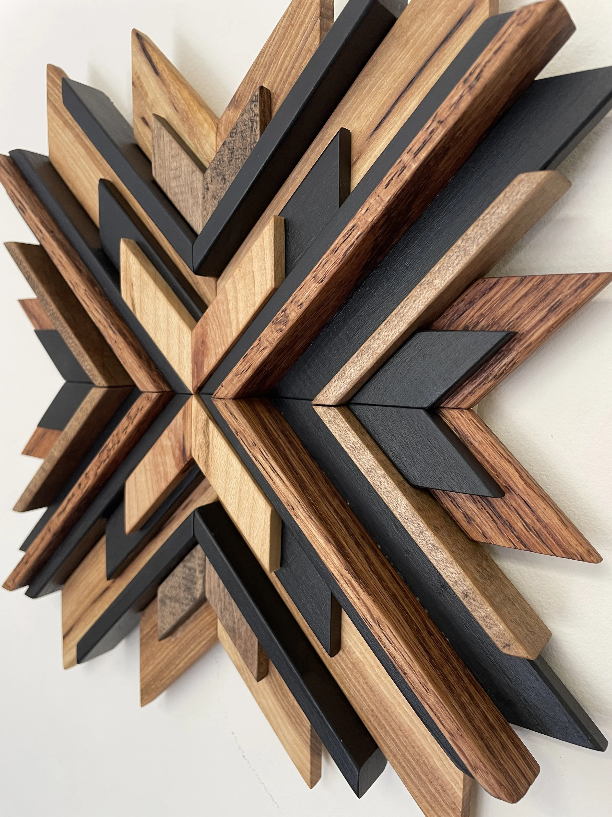 Angled view of a handcrafted sunburst style wooden mosaic in black paint with natural, espresso, and red mahogany stains.