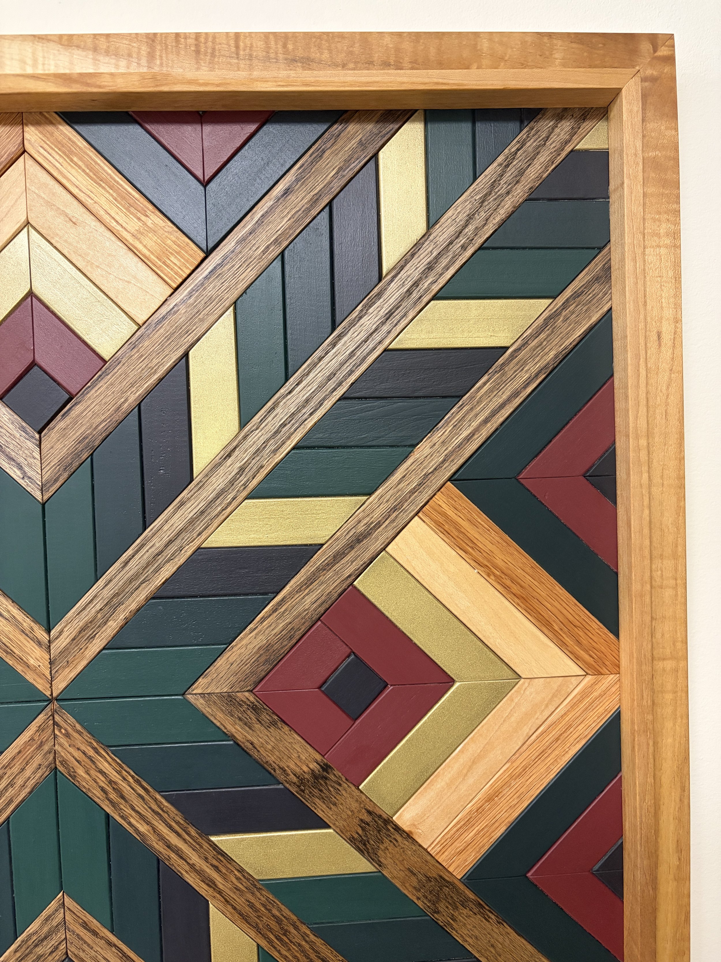 Close up view of a handcrafted framed wooden mosaic in black, gold, maroon, teal, and green paint with natural and espresso stains.