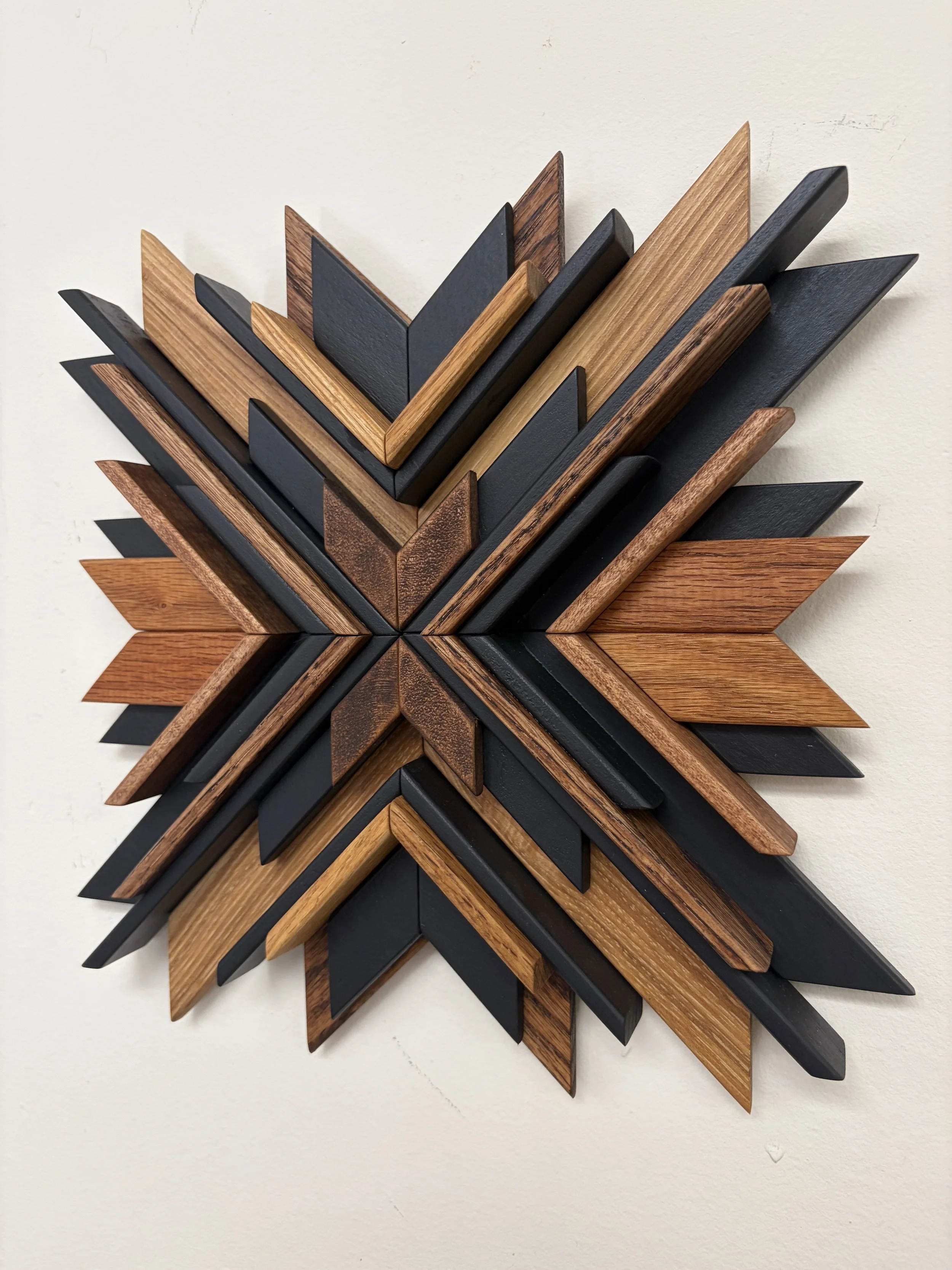 Angled view of a wooden sunburst style mosaic in black paint with light and dark stains.