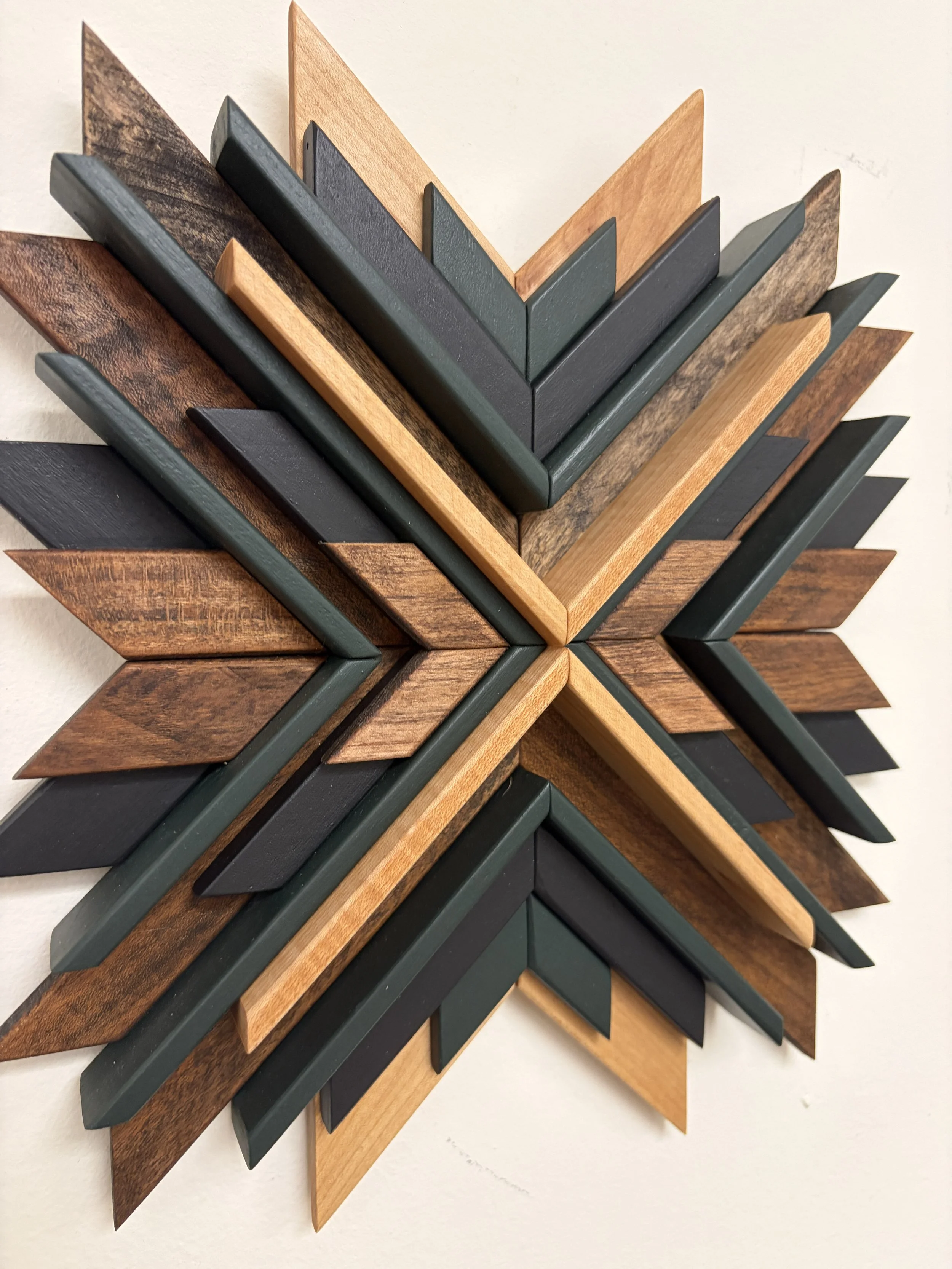 Angled view of a wooden sunburst style mosaic in black and green paint with natural and espresso stains.