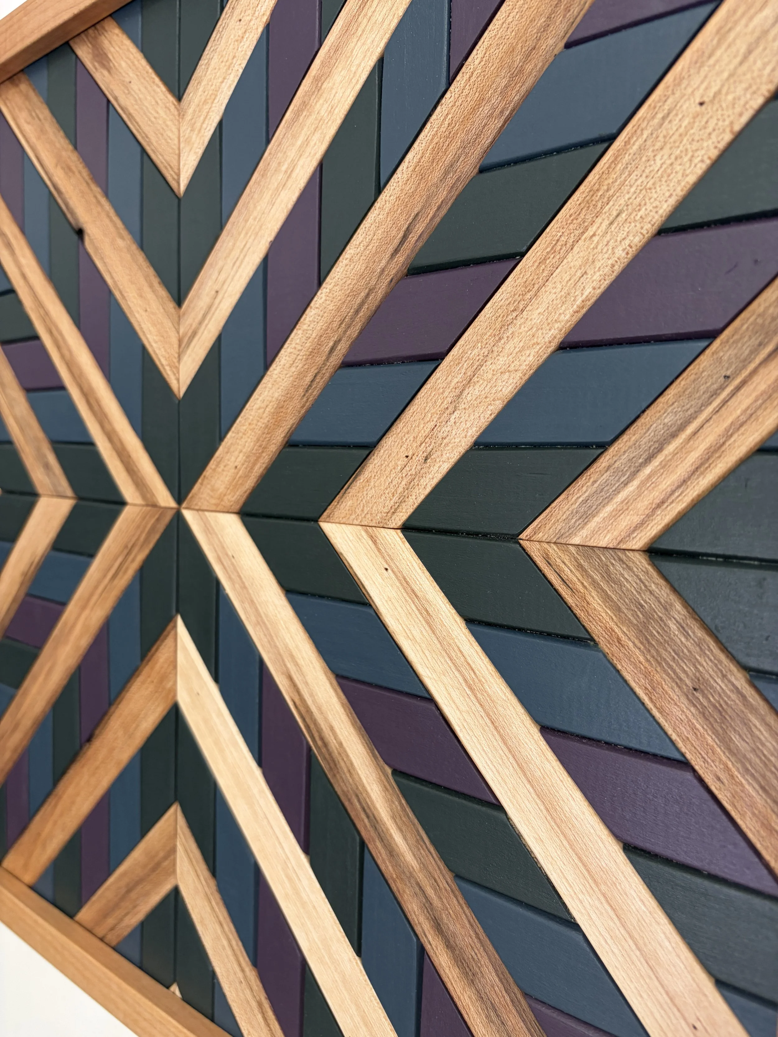 Close up view of a handcrafted framed wooden mosaic in green, purple, and blue paint with natural stains.