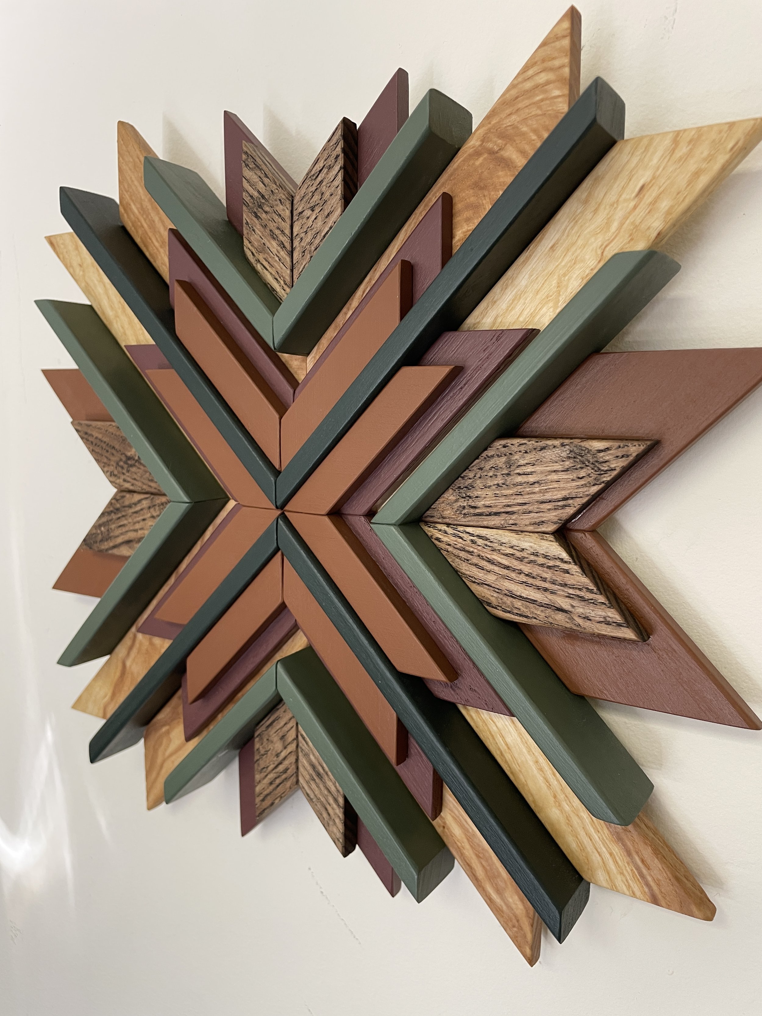 Side view of a handcrafted sunburst style wooden mosaic in pink, orange, and two  different green paints with natural and espresso stains.