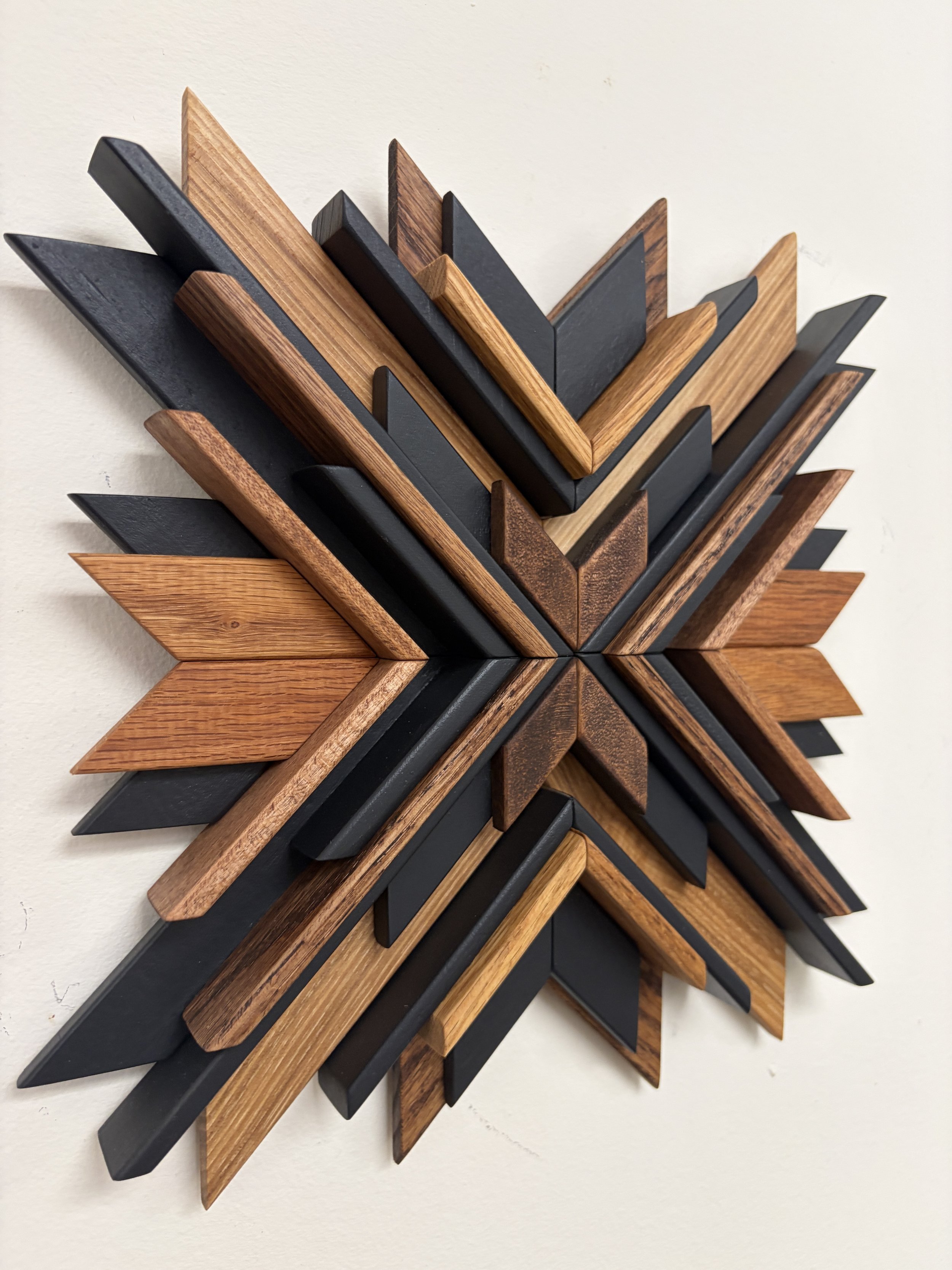 Side view of a wooden sunburst style mosaic in black paint with light and dark stains.