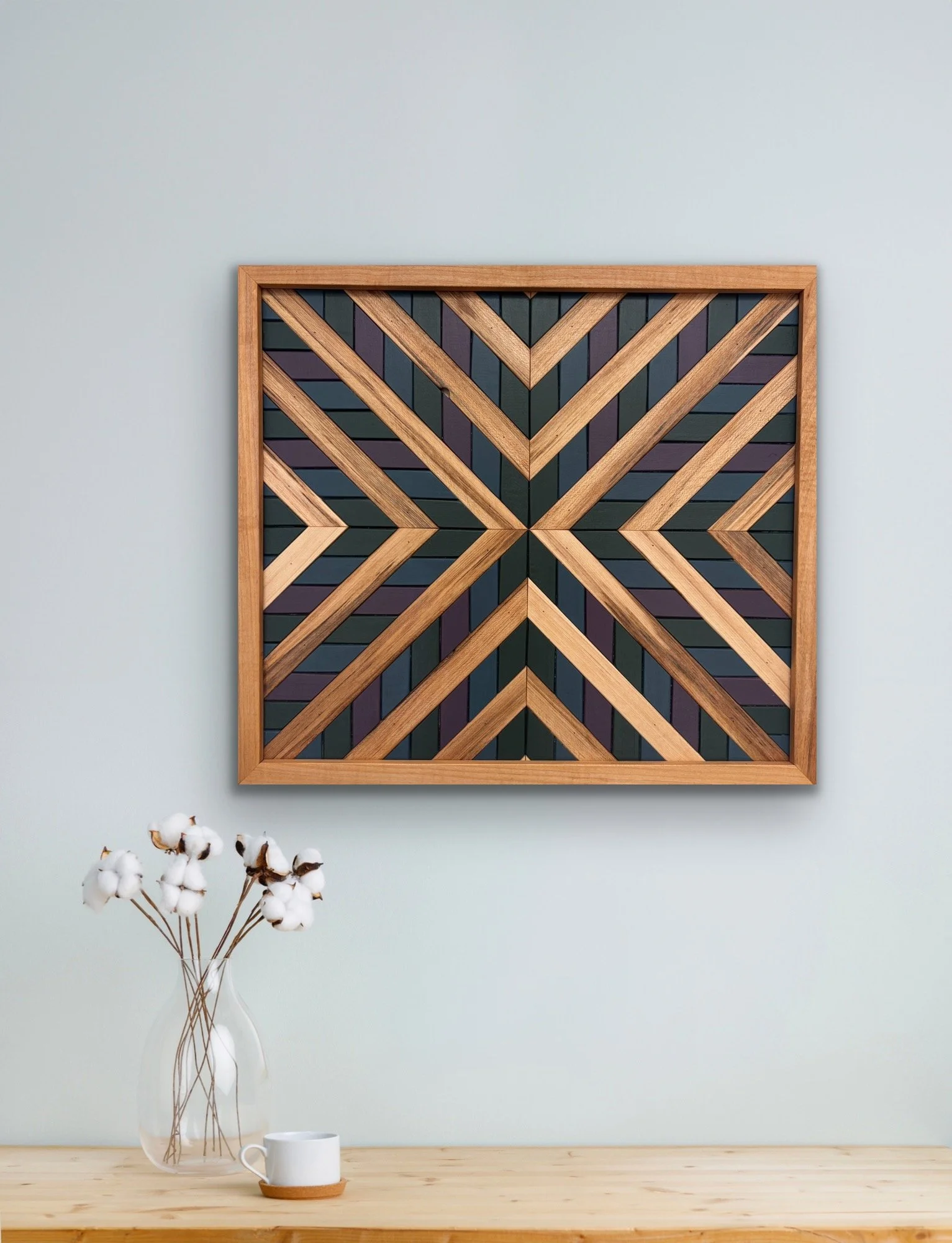 Handcrafted framed wooden mosaic in green, purple, and blue paint with natural stains displayed on a wall.