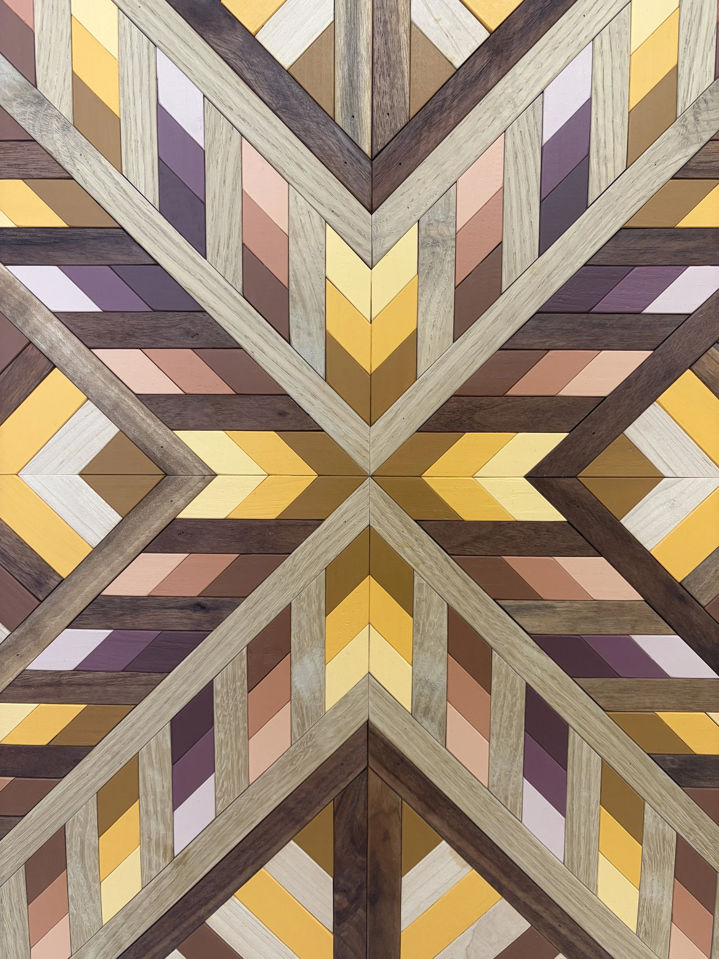 Zoomed in view of a handcrafted framed wooden mosaic in several shades of pink, orange, and yellow paint with natural stains.