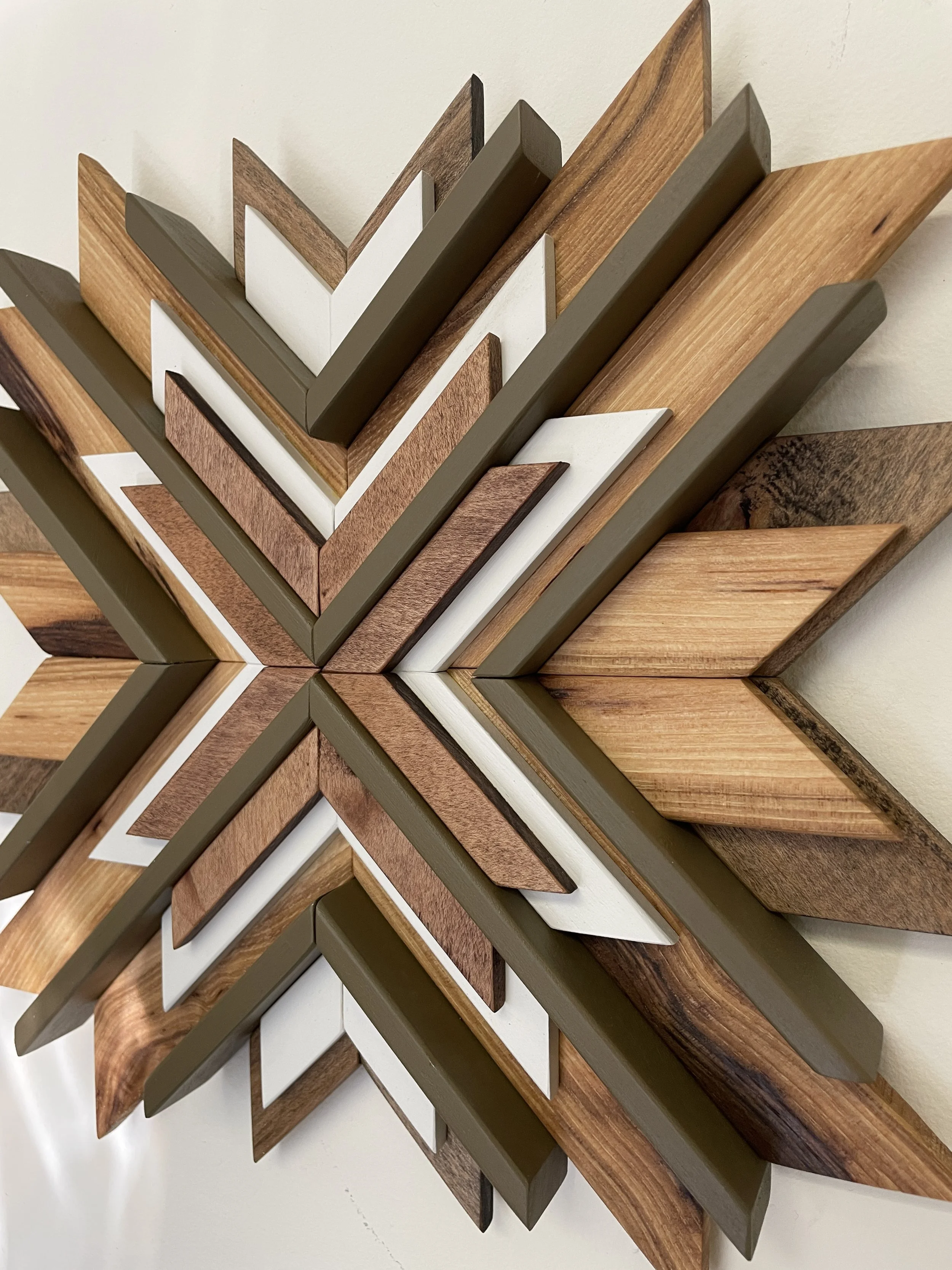 Close up side view of a handcrafted sunburst style wooden mosaic in white and green paints with natural and dark stains.