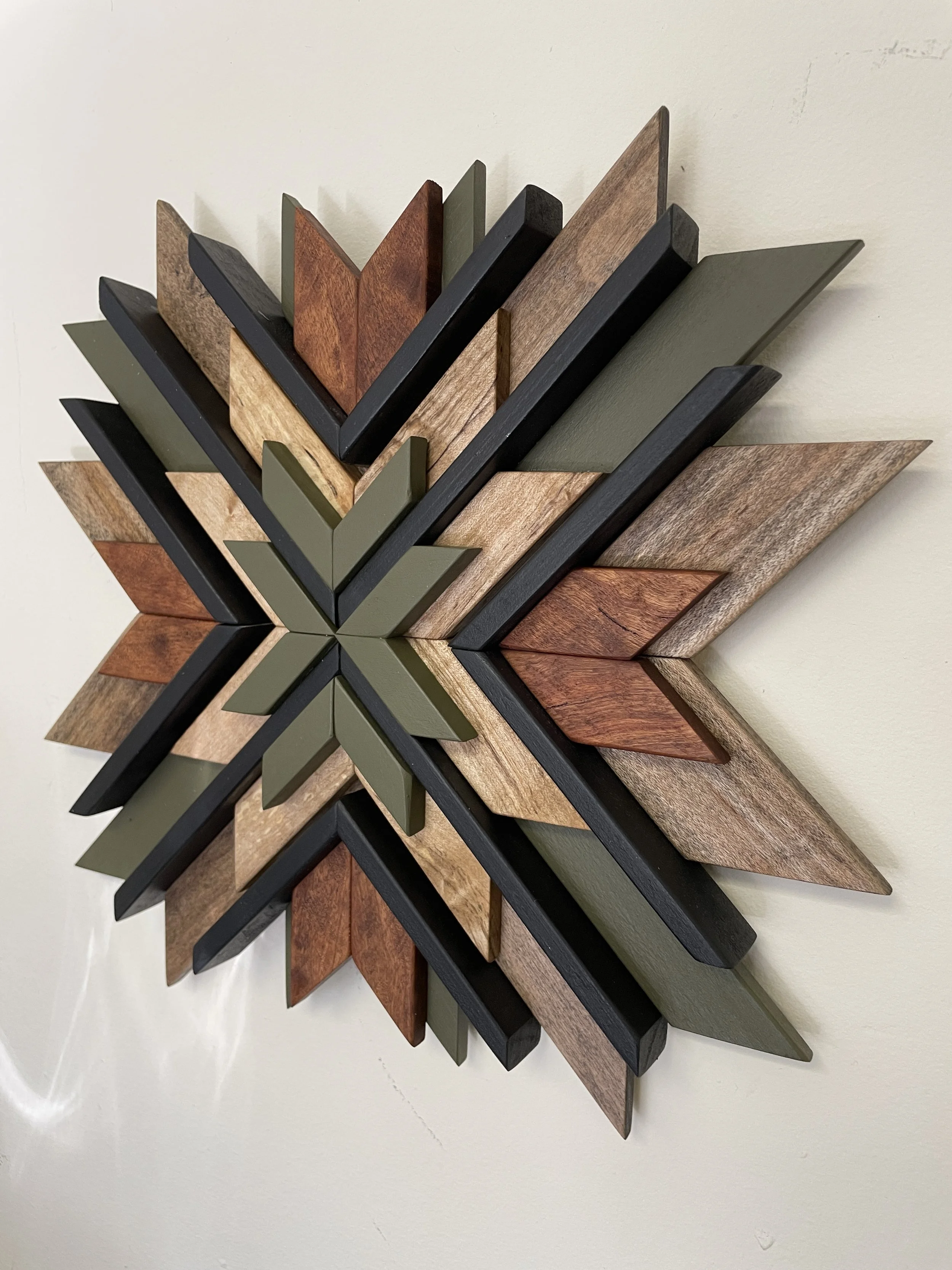Angle view of a handcrafted sunburst style wooden mosaic in black and green paint with natural and dark wood stains.