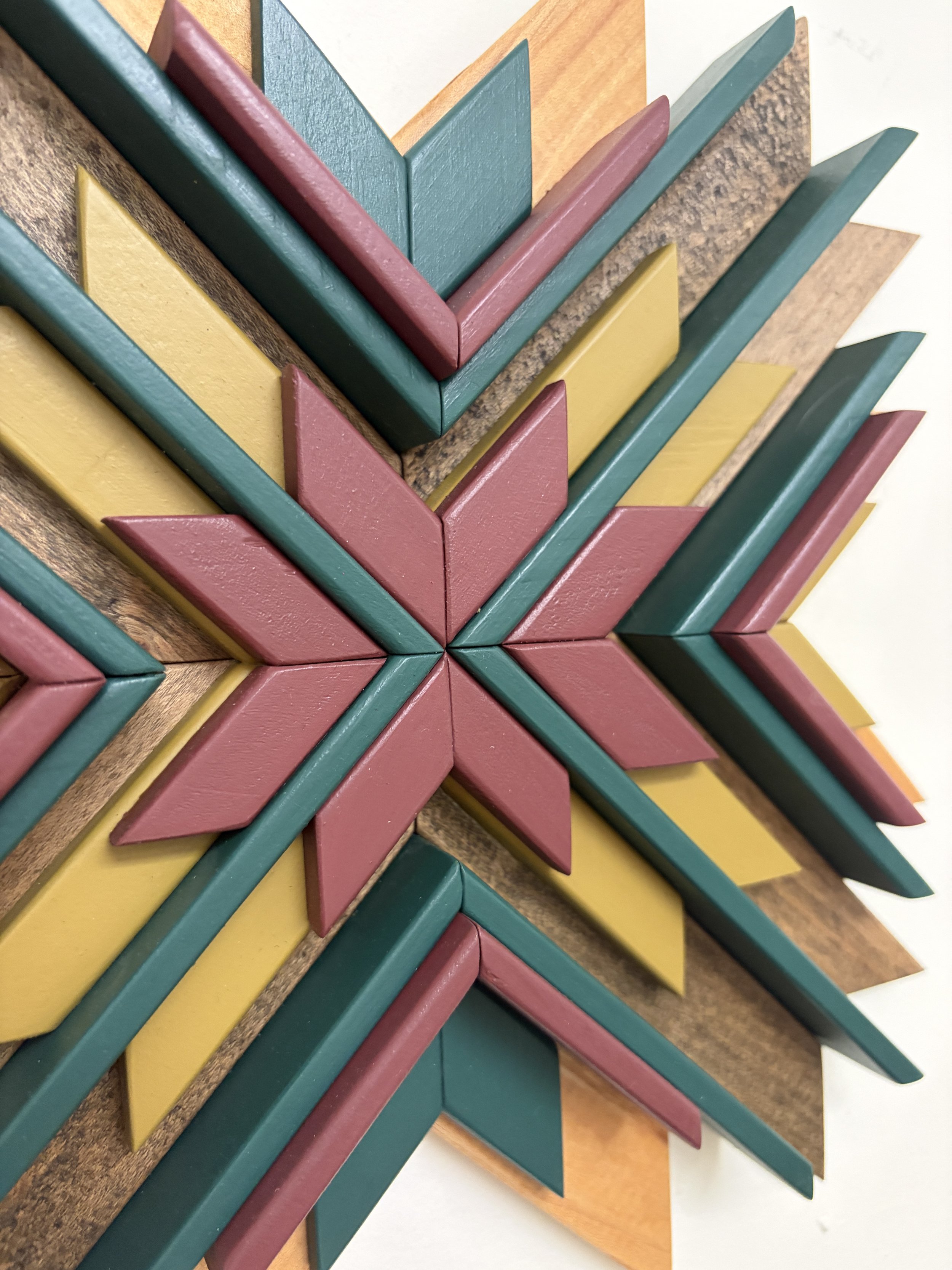 Close up view of a sunburst style wooden mosaic in pink, teal, and bright green paint with natural and espresso stains.