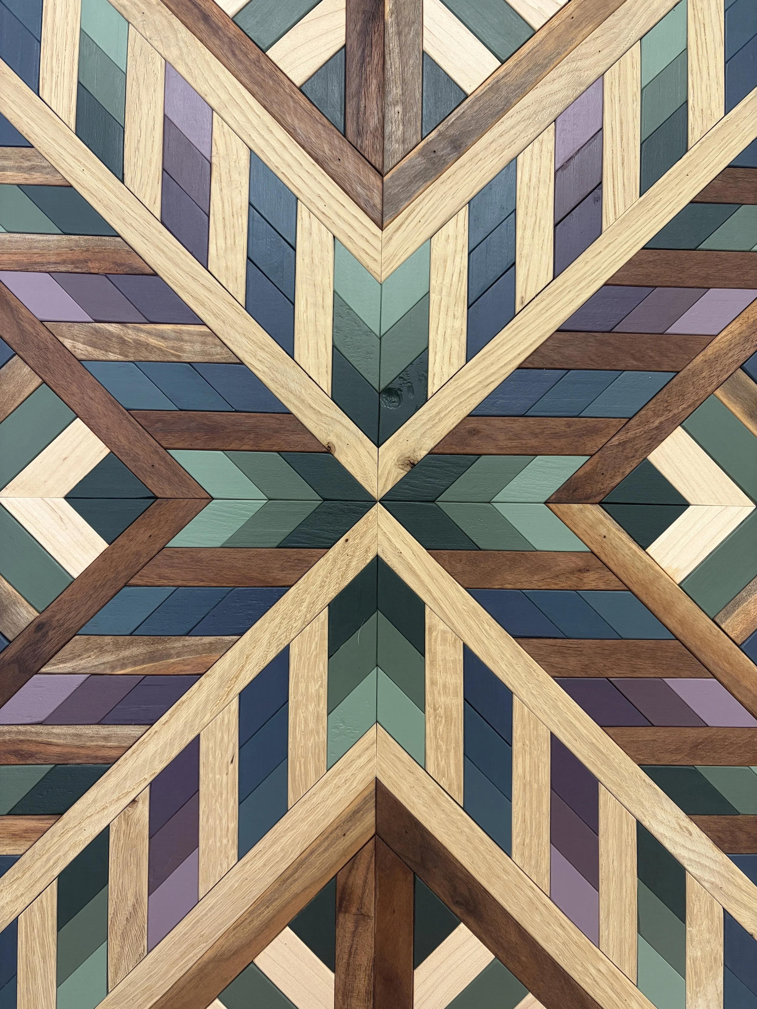 Zoomed in view of a framed wooden mosaic in several shades of blue, green, and purple paint with natural stains.