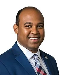 Portrait of a man wearing glasses, a suit, and a tie, labeled as President Mr. Manuel Martinez, Jr. in front of a bridge background.