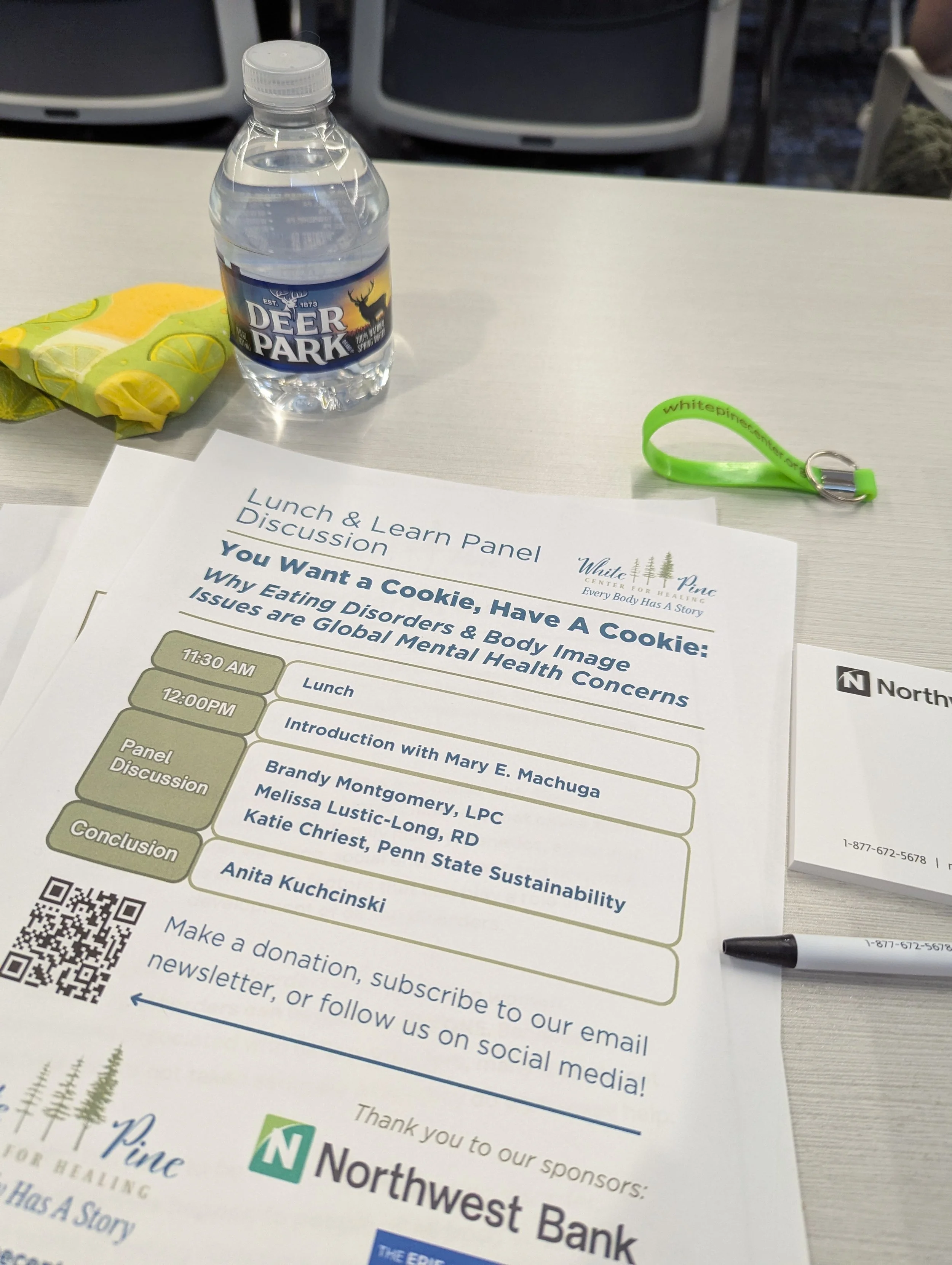 A table with a water bottle, a green wristband, a pen, and a paper with a schedule for a lunch and learning panel discussion about eating disorders and mental health.
