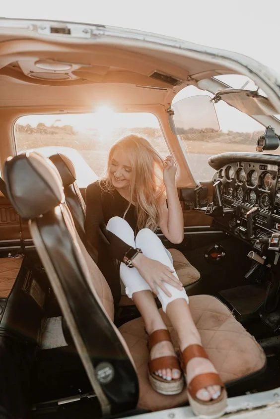 Sit naturally in the cockpit and tuck your legs in comfortably. Look down and laugh softly, like you’re having a quiet moment before takeoff. Then brush your hair back and glance out the window