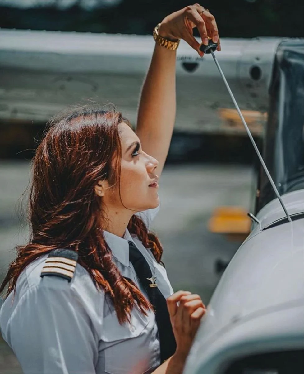 Act like you’re doing your preflight. Reach toward the aircraft slowly and focus on what you’re checking. Don’t worry about smiling yet Reach, pause, look at the detail, then glance slightly toward me without fully posing.”
