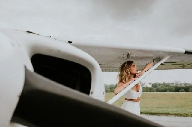 Pose direction:
“Stand under the wing and bring one arm up to the strut or wing area. Stretch your body long, shift your weight into one hip, and lift your chin slightly toward the light.”

Movement cue:
“Reach up slowly, then let your body settle in