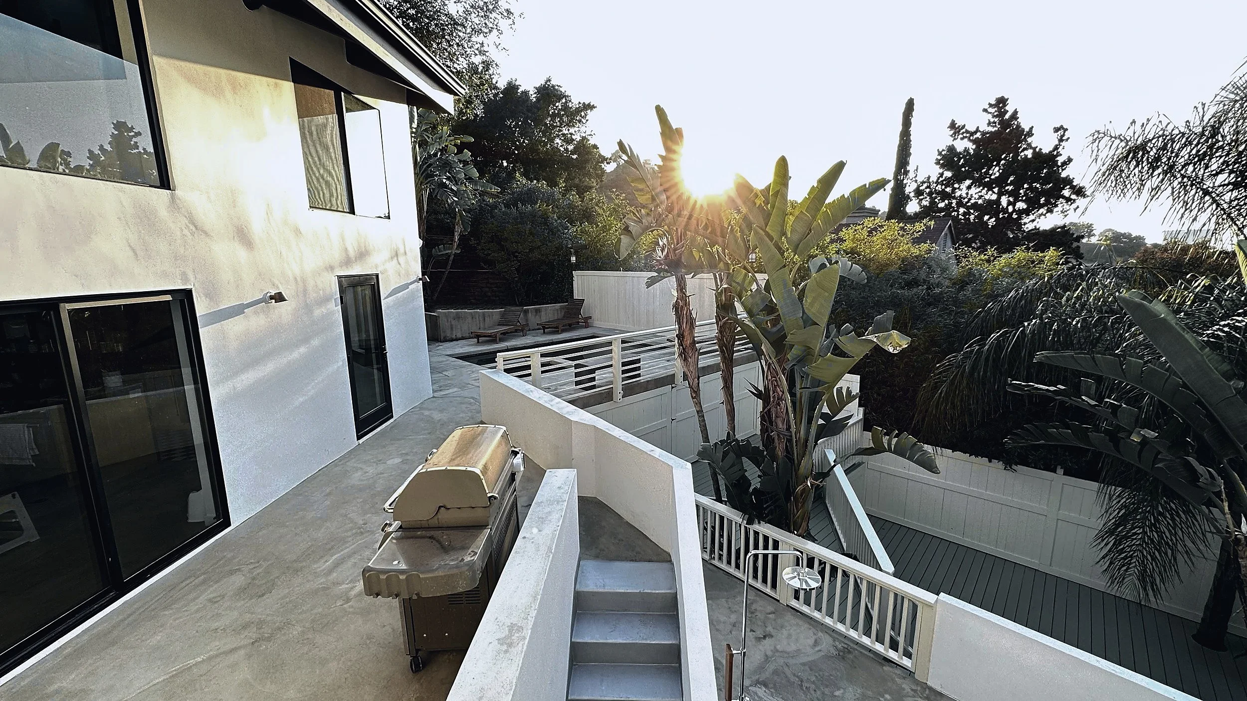 Upper concrete terrace beside stucco walls and sliding doors, with stairs down to the deck.