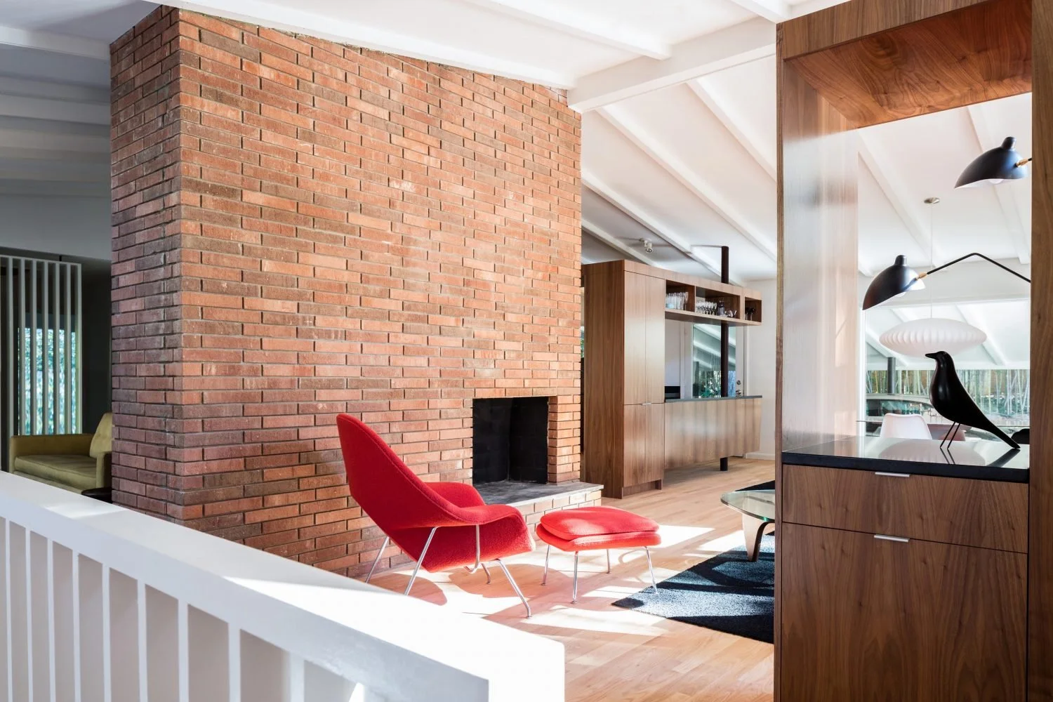 Mid-century modern living room with a red chair, brick fireplace, wooden cabinetry, and black decorative bird sculpture.