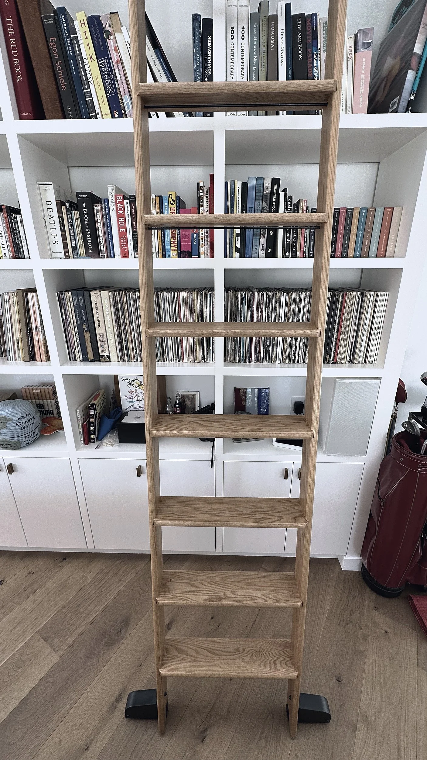 Oak rolling ladder standing against white shelving filled with art books and vinyl records.