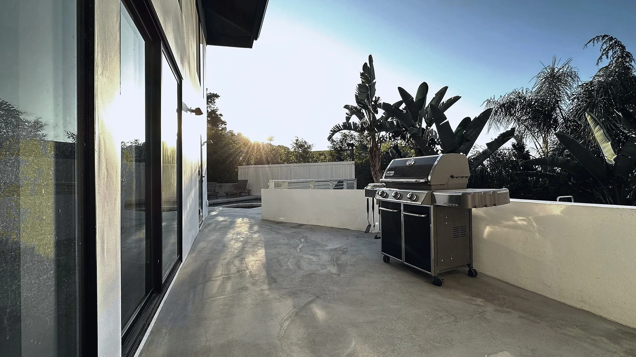 Concrete terrace running along sliding glass doors, with a gas grill at the low wall.