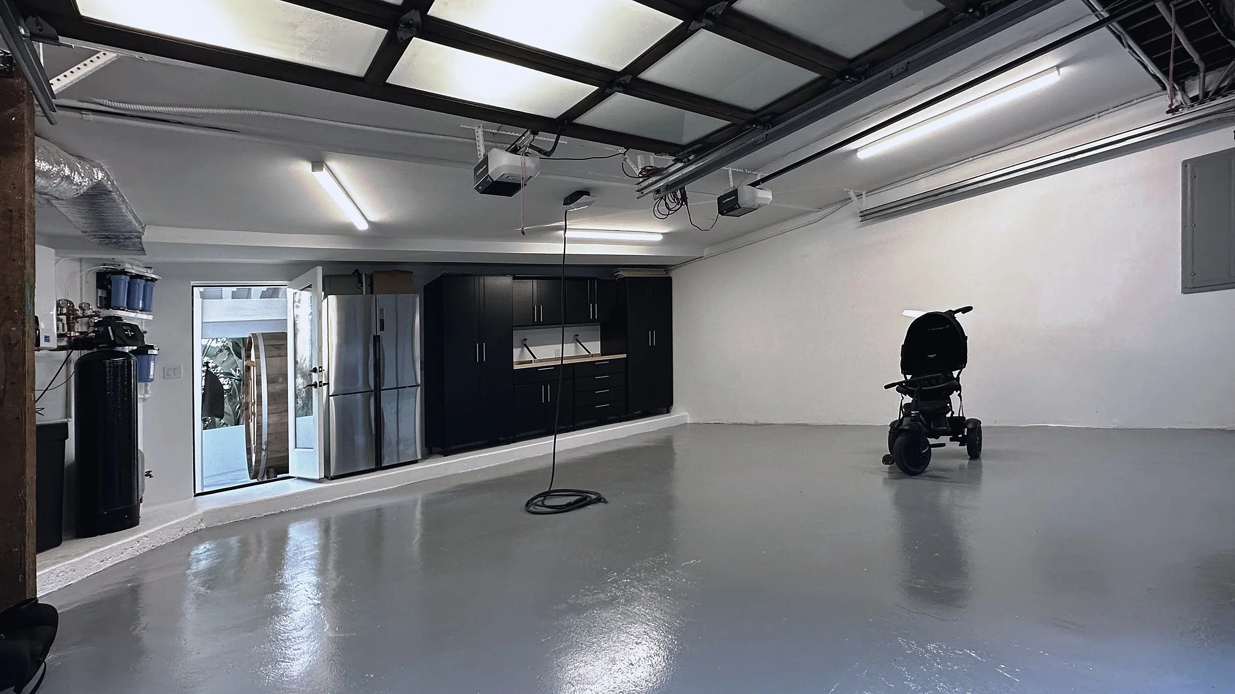 Garage with a coated concrete floor, black storage cabinets, and a glazed overhead door.