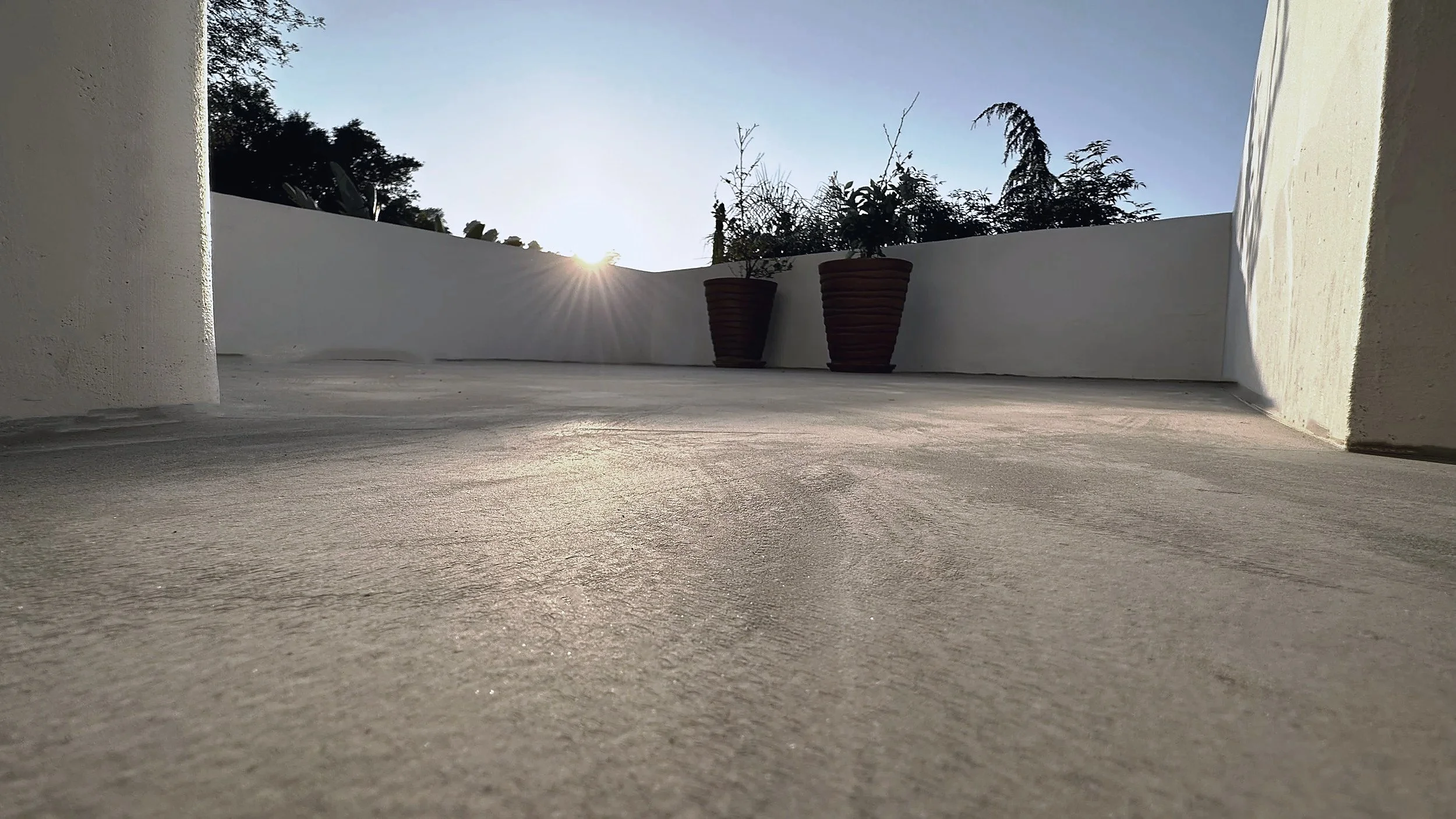 Enclosed concrete courtyard bounded by white stucco walls, with two terracotta planters.