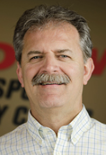 Smiling man with mustache in plaid shirt, indoor setting.