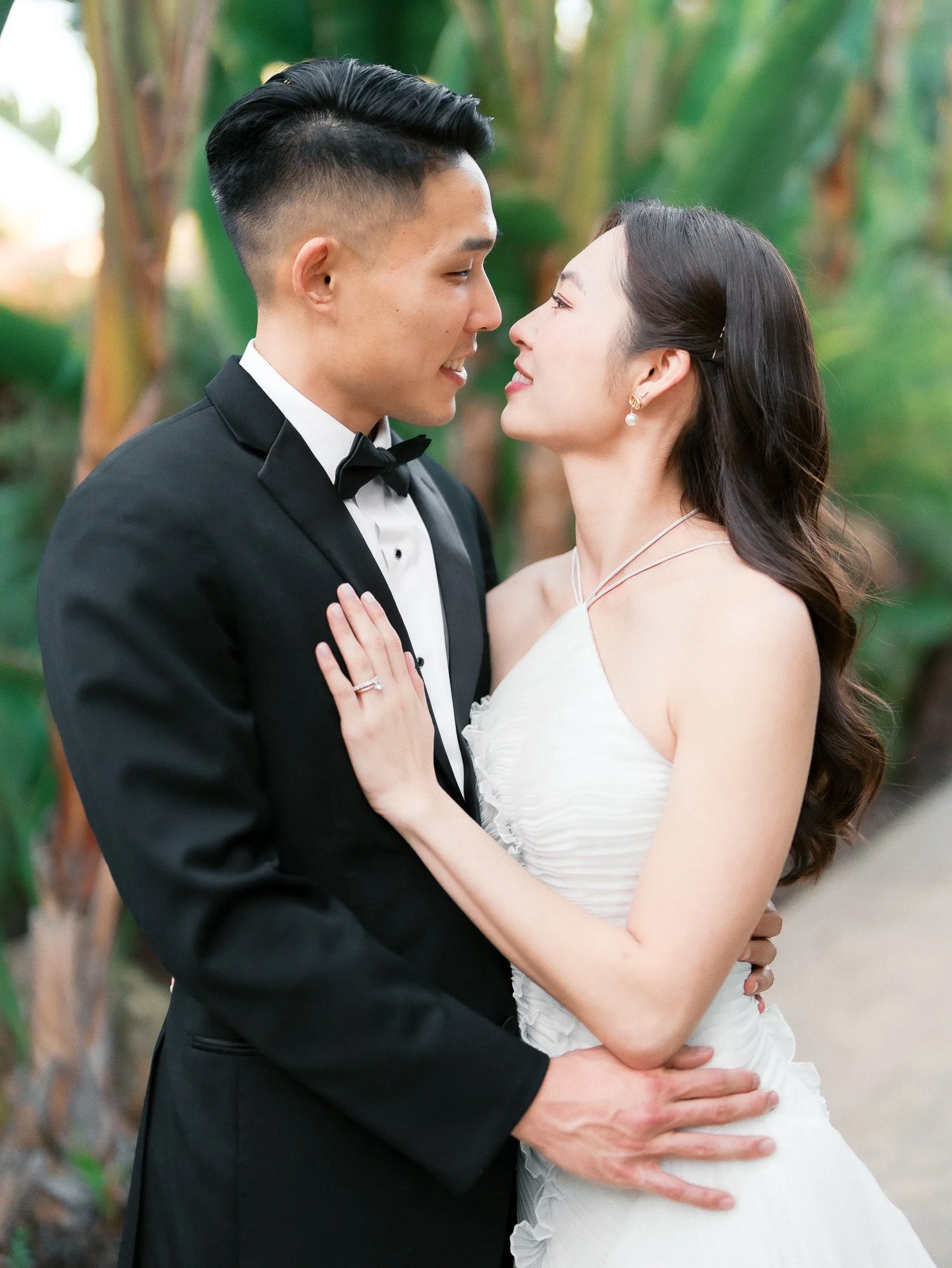 A bride and groom in wedding attire sharing an intimate moment outdoors surrounded by greenery.
