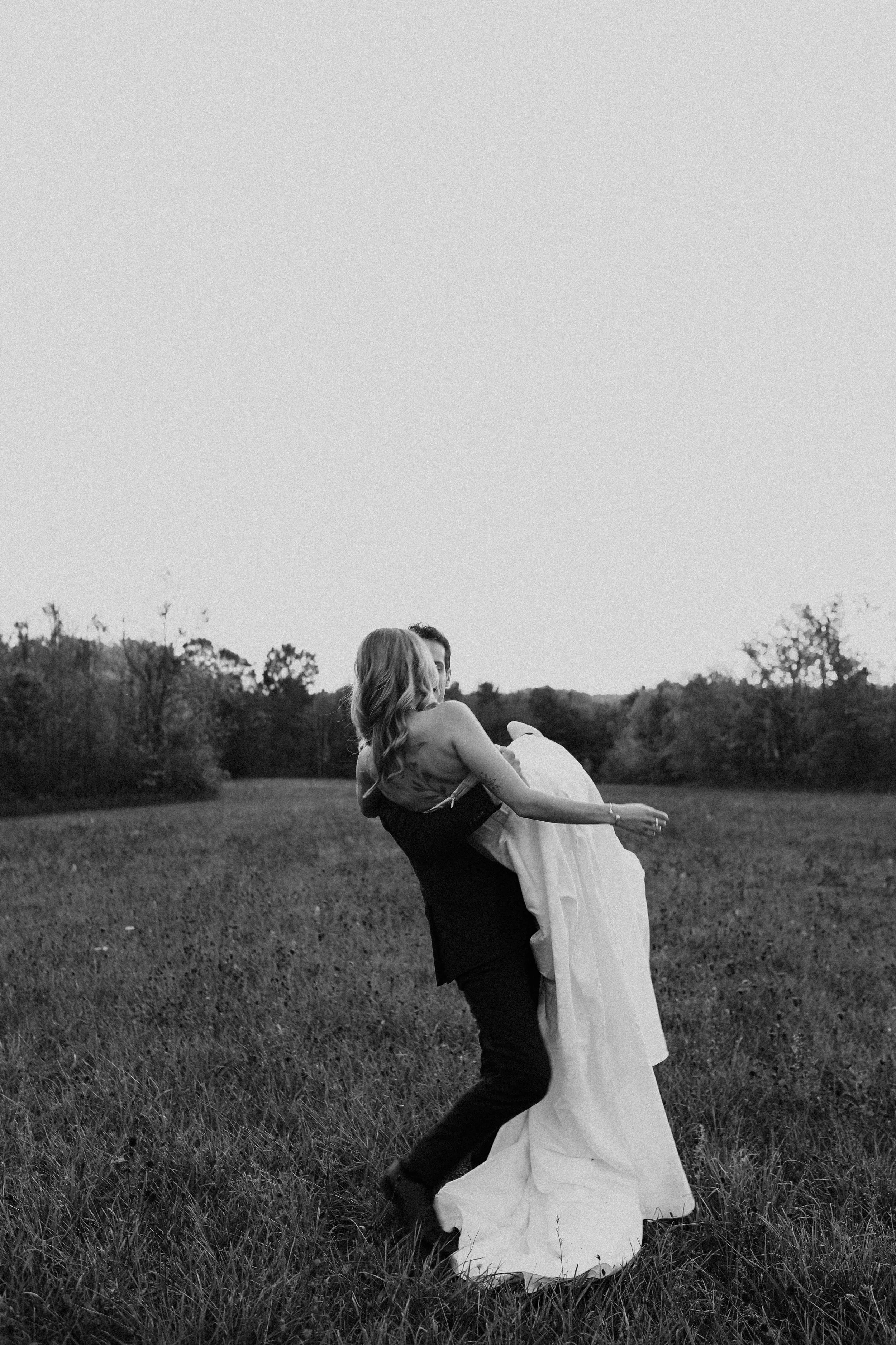 Bride and groom in field holding each other 