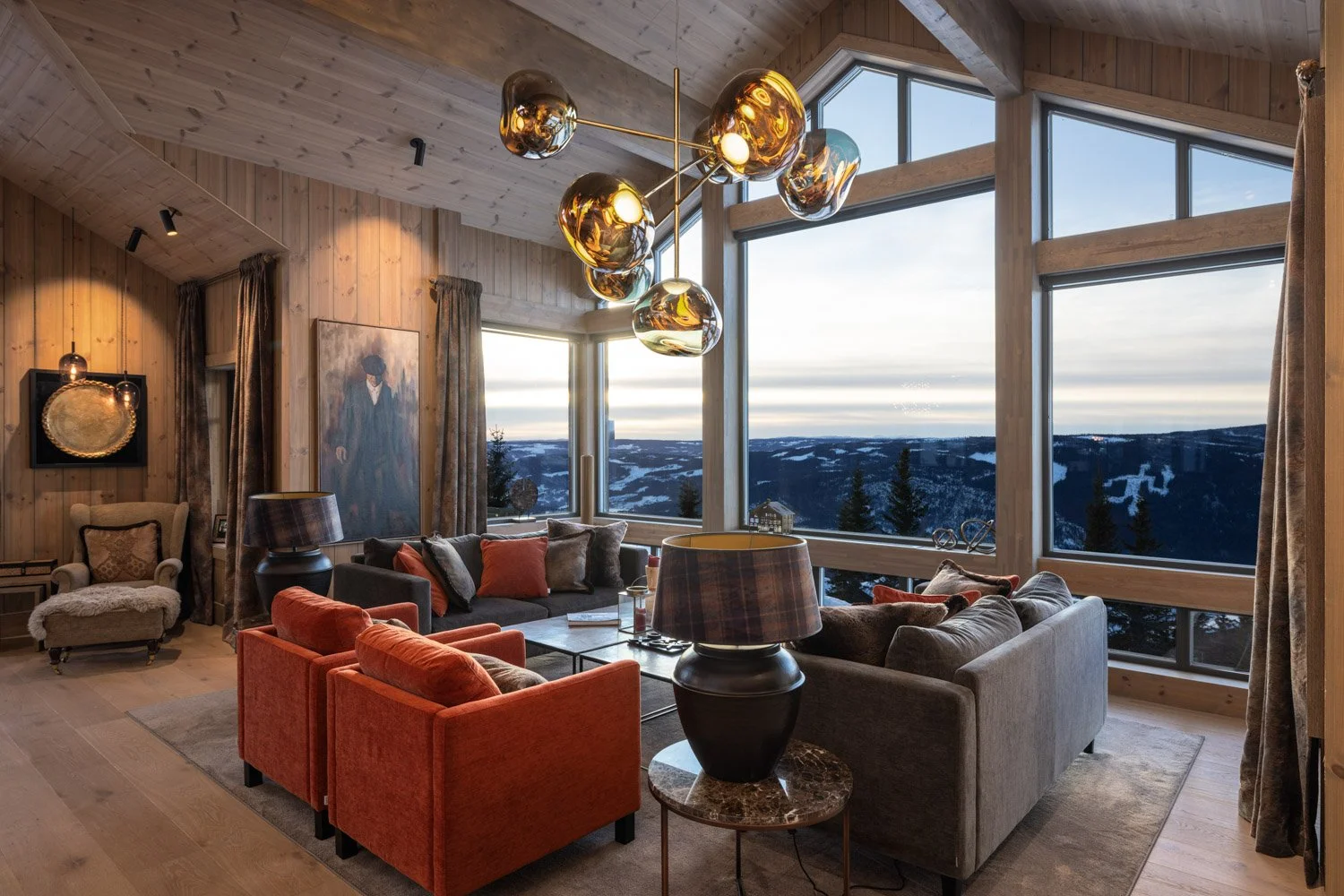 Innendørs stue med store vinduer som viser fjellandskap, sofaer og salongbord, samt pynt- og lampedekorasjoner.