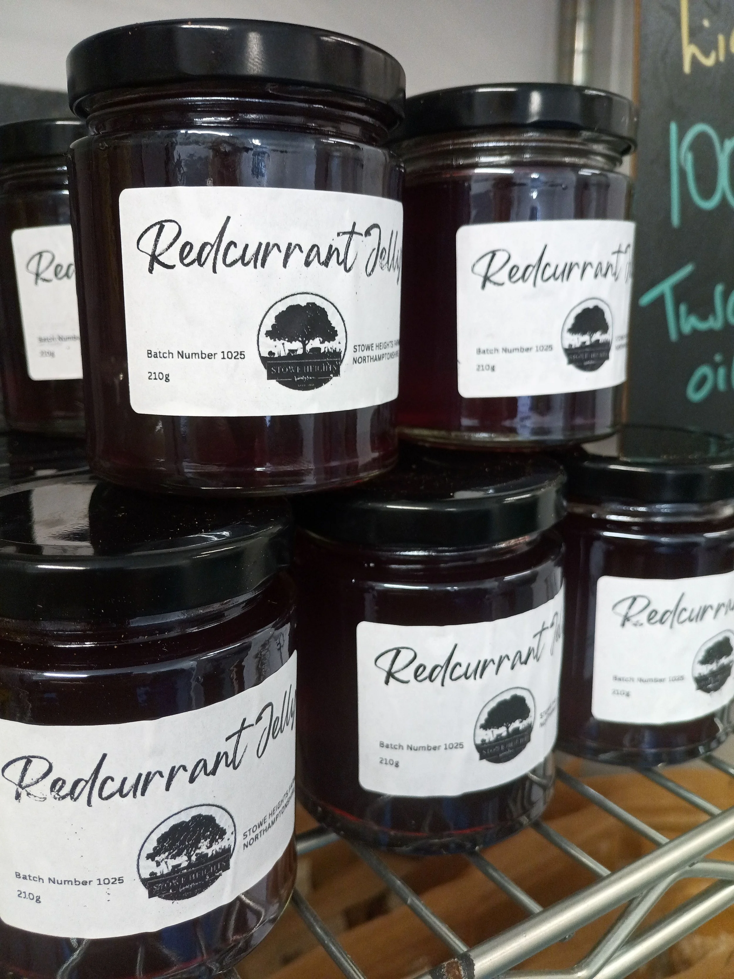 Jars of redcurrant jelly displayed on a wire shelf with labels showing batch number and weight.