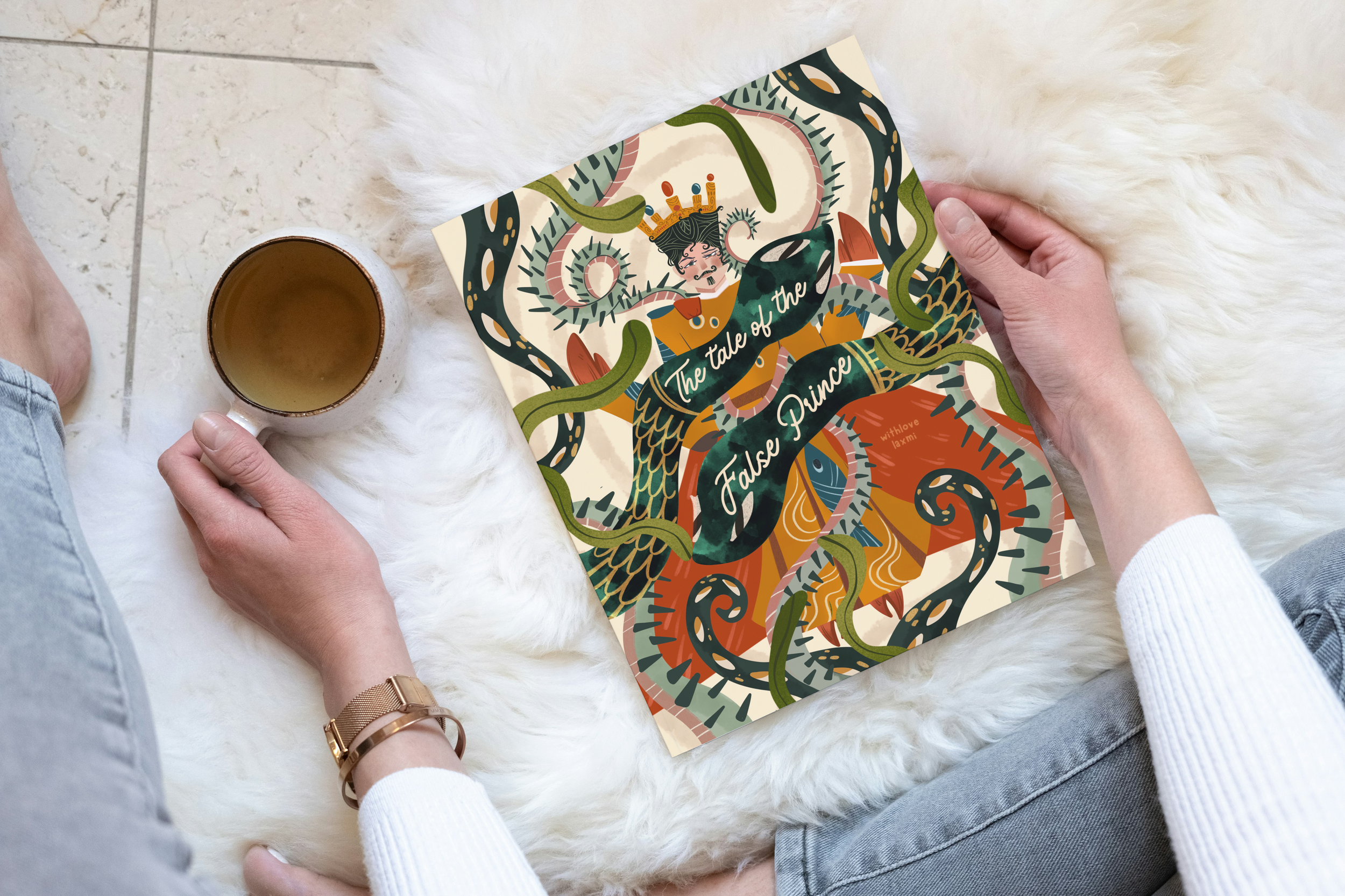 A person sitting on a white furry rug holding a book titled 'The Tale of the False Prince' with a cup of tea beside them.
