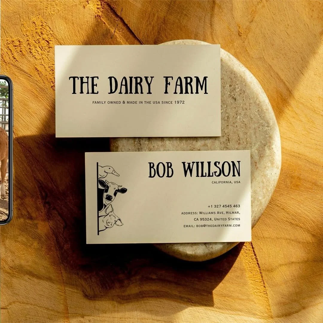 Business cards for The Dairy Farm and Bob Willson are placed on a rounded stone on a wooden surface.