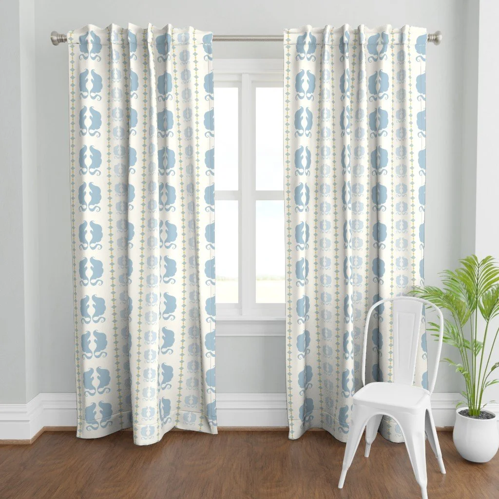 Decorative curtains with a blue and white pattern hanging in front of a window, with a white chair and a potted plant in a bright room.