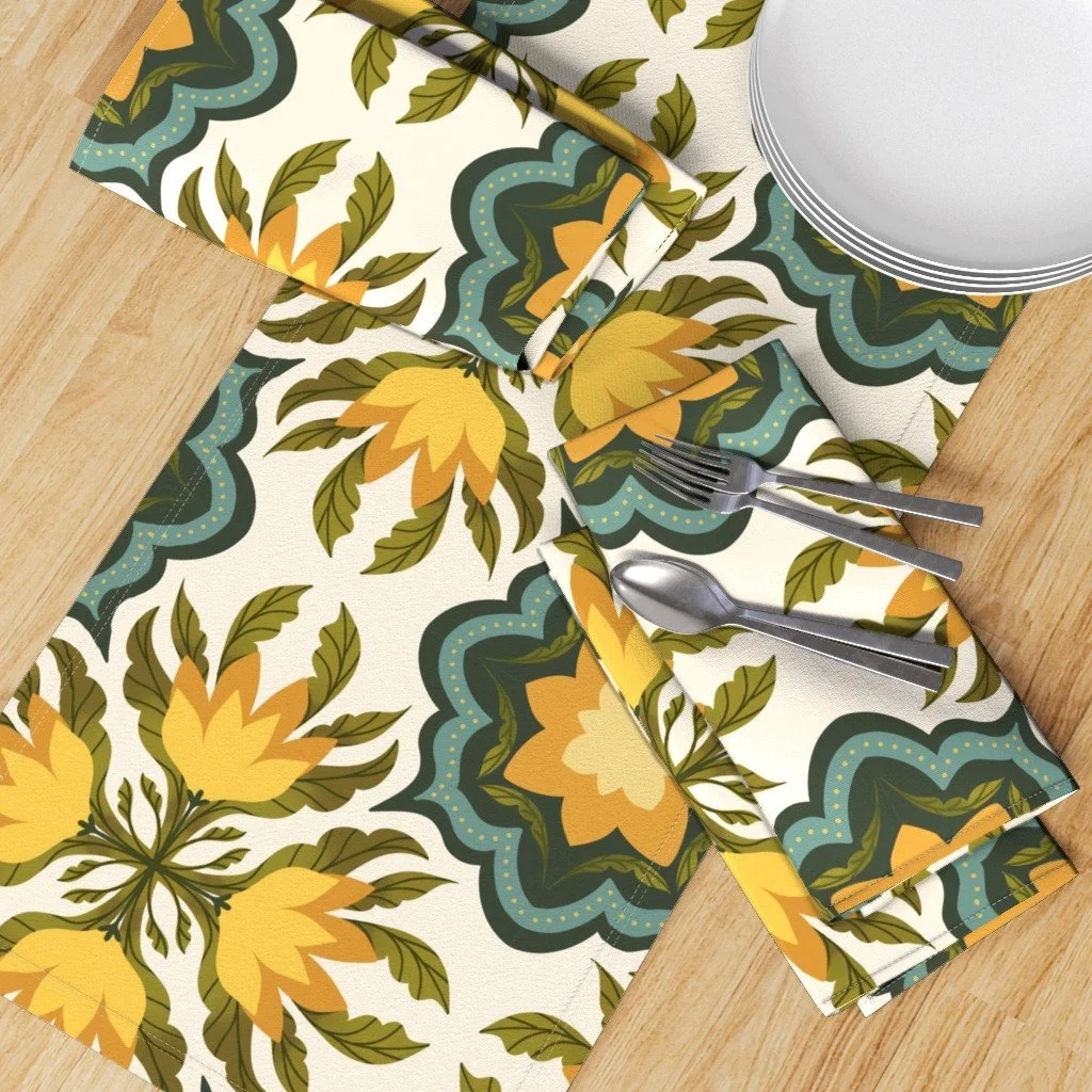 A table setting with a floral-patterned tablecloth, napkin, and placemats featuring yellow and green floral designs, along with a set of forks and spoons and a stack of white plates.