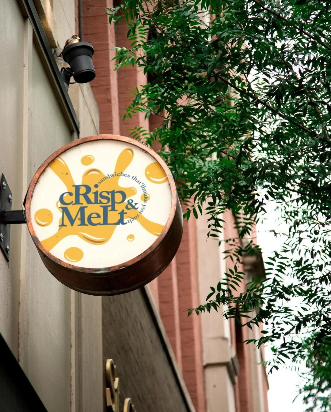 Circular outdoor sign for 'Crisp & Melt' featuring a yellow cheese splash design with the tagline 'sandwiches that will make your day'.