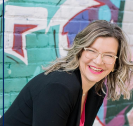 Smiling person with glasses in front of colorful graffiti wall.