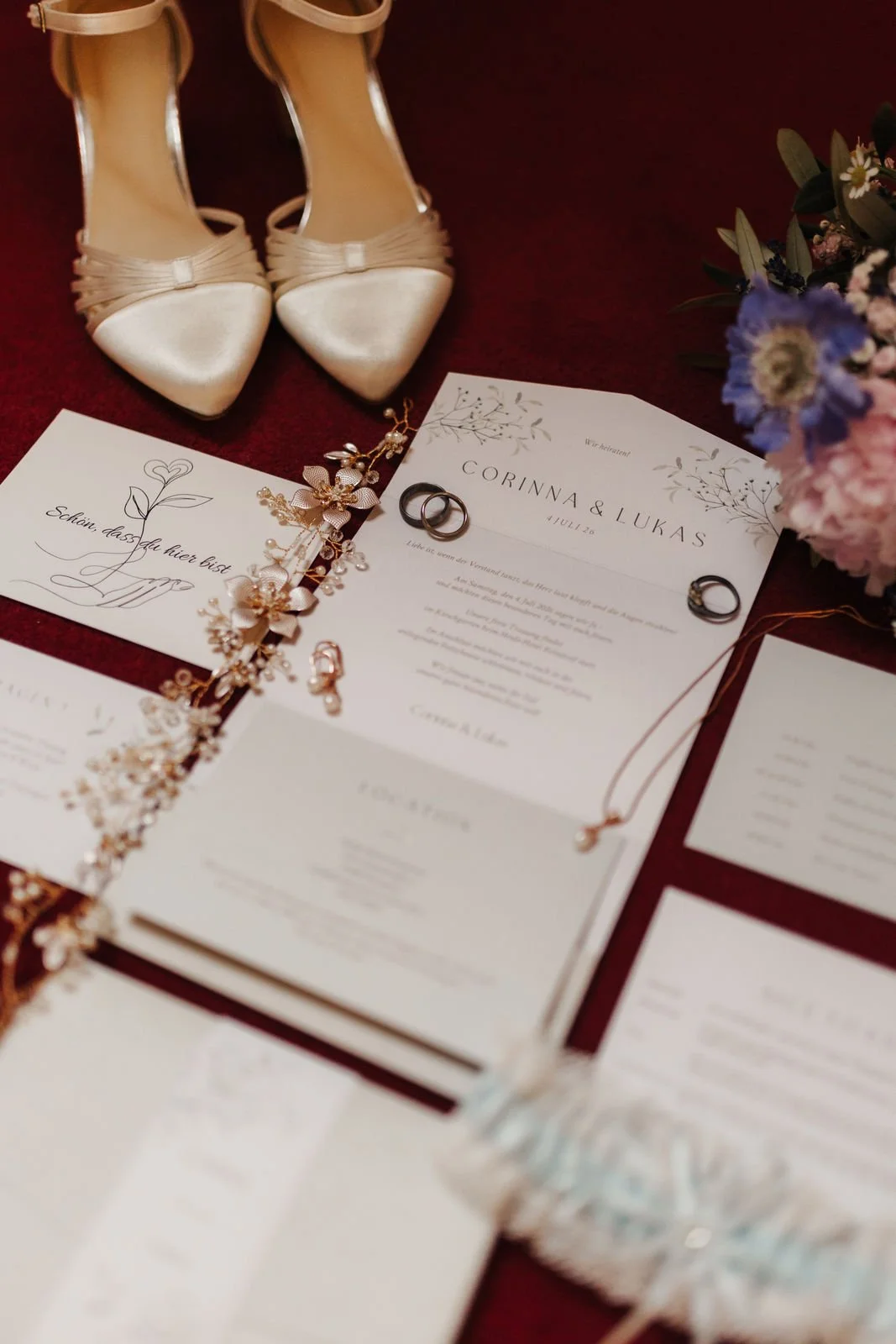 Liebevoll arrangierte Hochzeitsdetails mit weißen Brautschuhen, Eheringen, Einladungskarten, goldenem Haarschmuck und Brautstrauß im Heide Hotel Reinstorf bei Lüneburg.