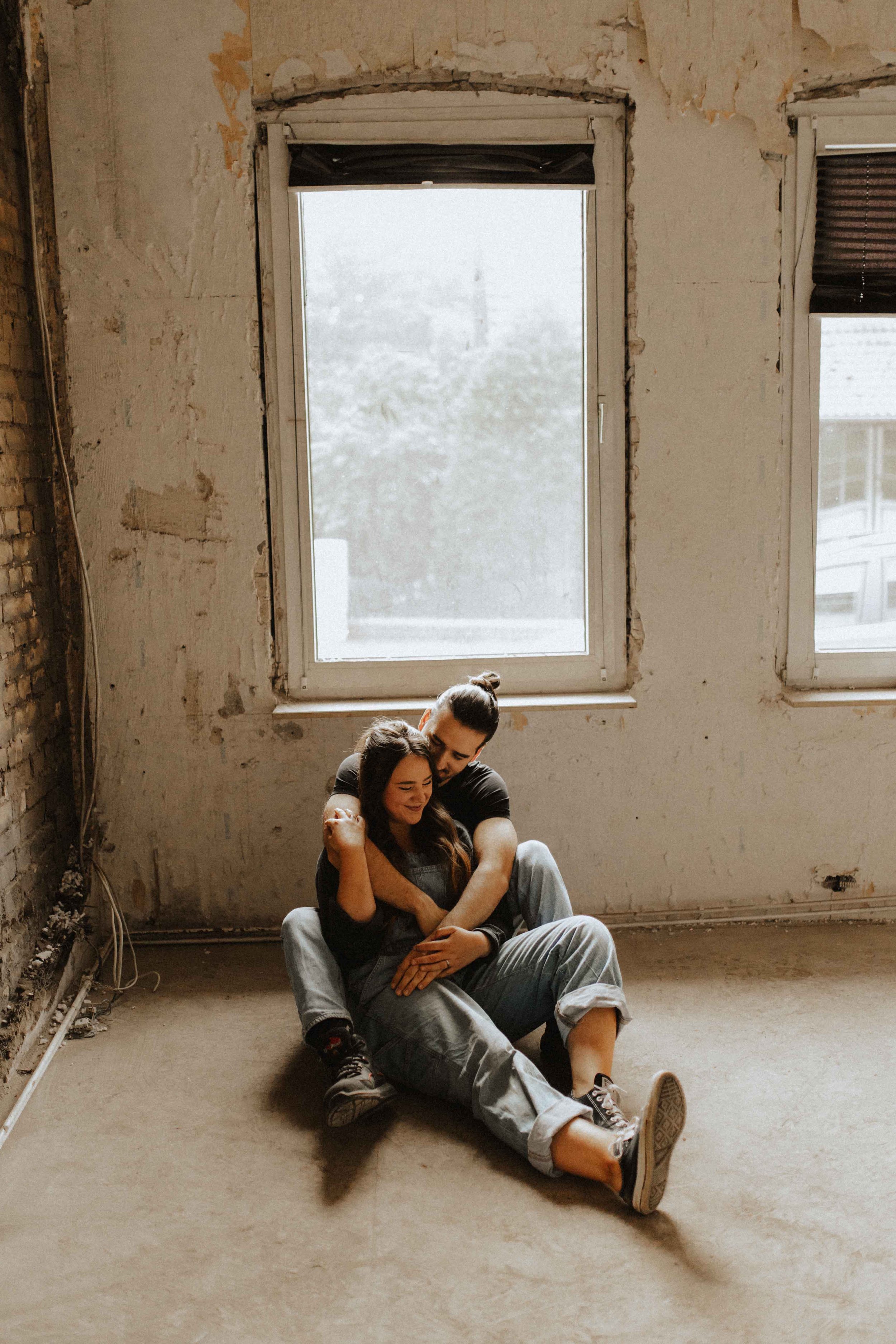 Paarshooting auf Baustelle – verliebtes Paar sitzt kuschelnd auf dem Boden vor einem alten Fenster in Lüneburg.  Du