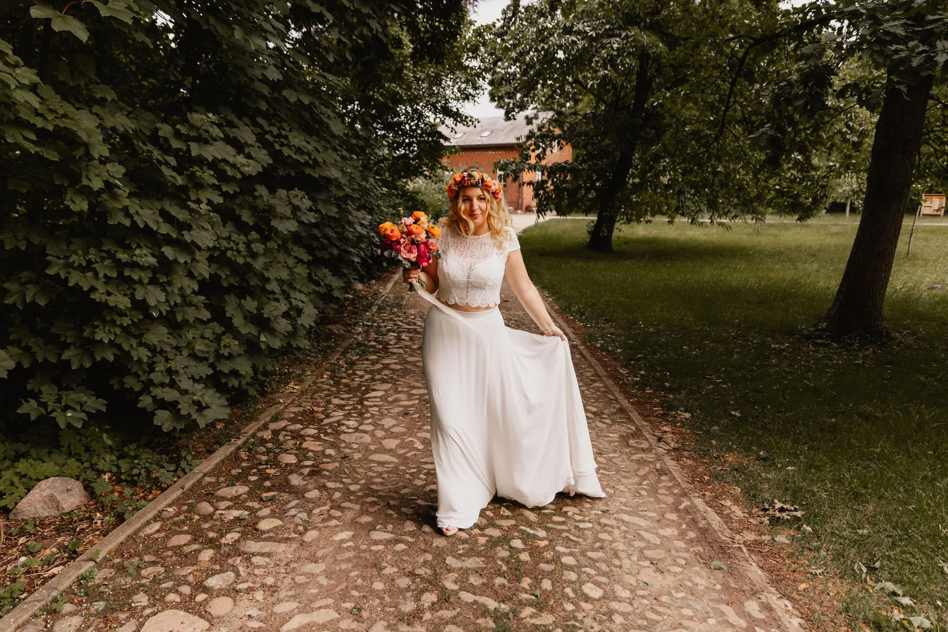 Braut mit Blumenstrauß und Hochzeitskleid posiert lächelnd auf einem Weg im Grünen in Lüneburg